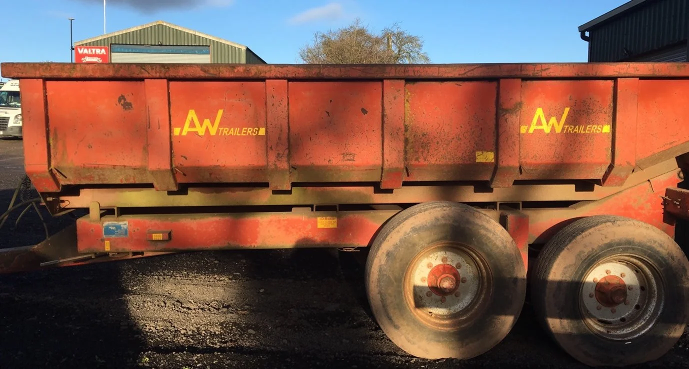 Red utility trailer with yellow logos, parked outdoors with a building and trees in the background.