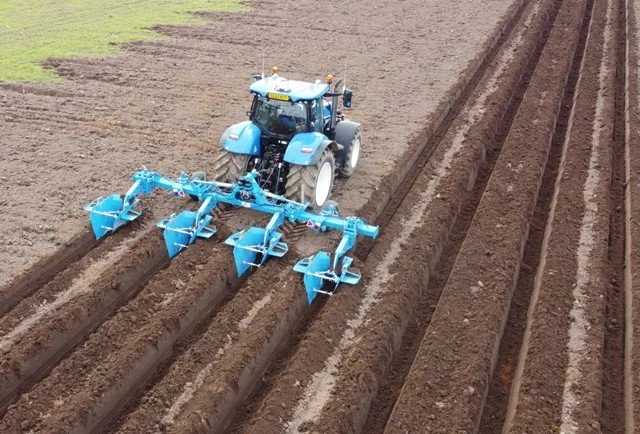 Blue tractor plowing fields with multiple furrows in dirt farm soil.