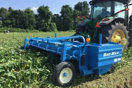 A blue Baumann implement attached to a tractor in a field