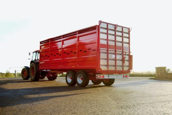 Red tractor pulling a large, enclosed red trailer in an open outdoor area.