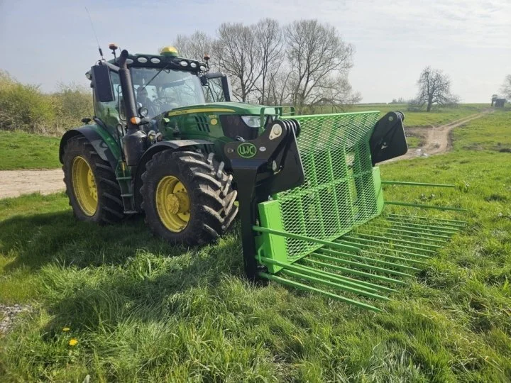 Green and black tractor with a green attachment on a grassy field under a partly cloudy sky.