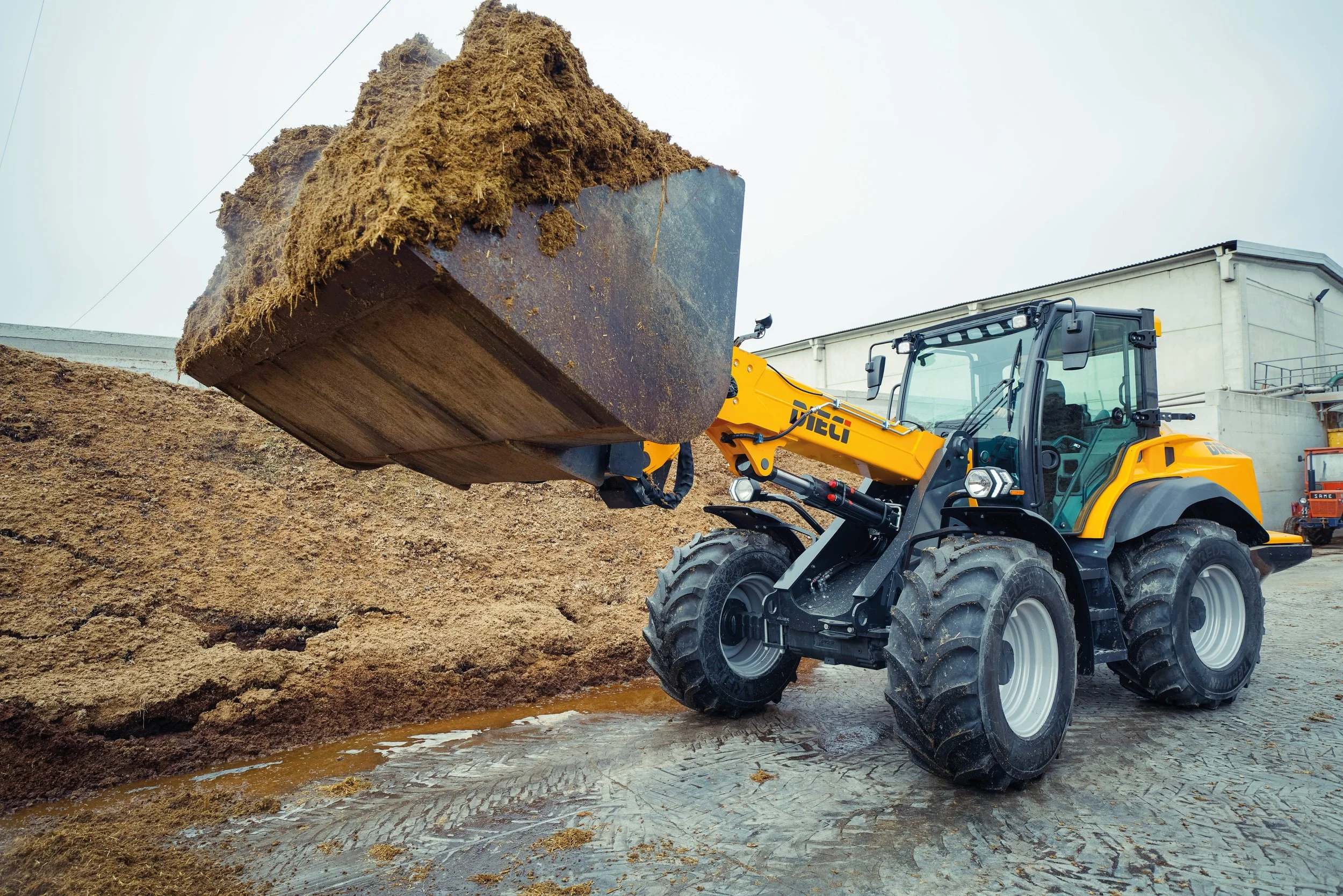 A yellow front-end loader moving brown dirt and mud.