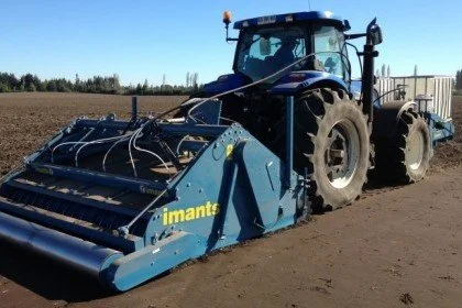 Blue tractor with an attached landscaping attachment on a dirt field.