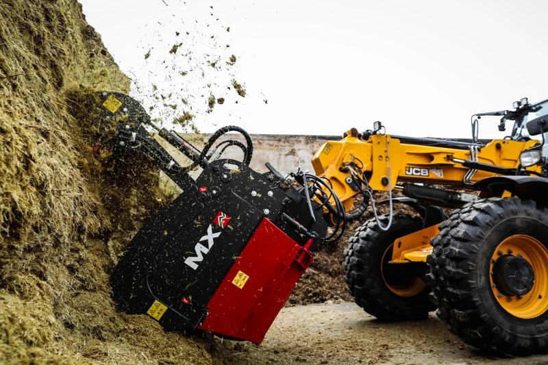 A yellow JCB wheel loader using an MX mulcher to clear a large pile of dirt or debris.