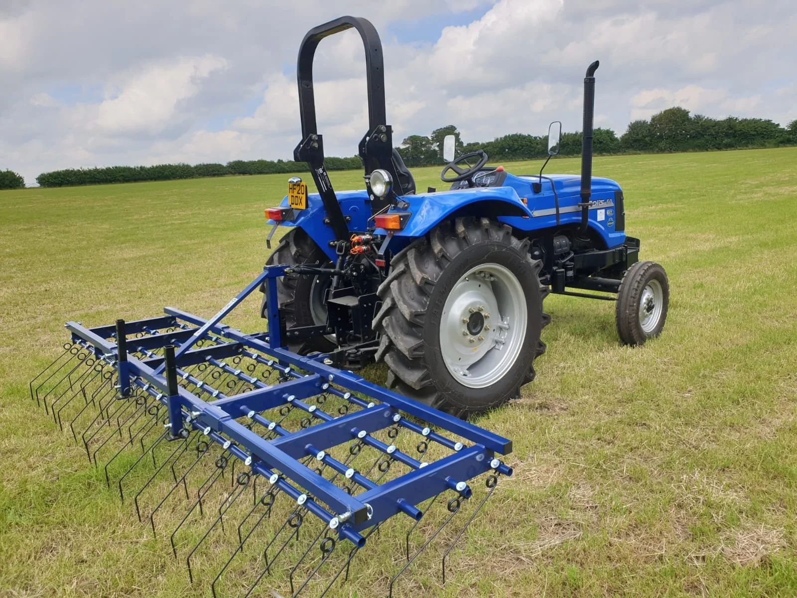 Blue tractor with a front attachment in an open grassy field under a partly cloudy sky.