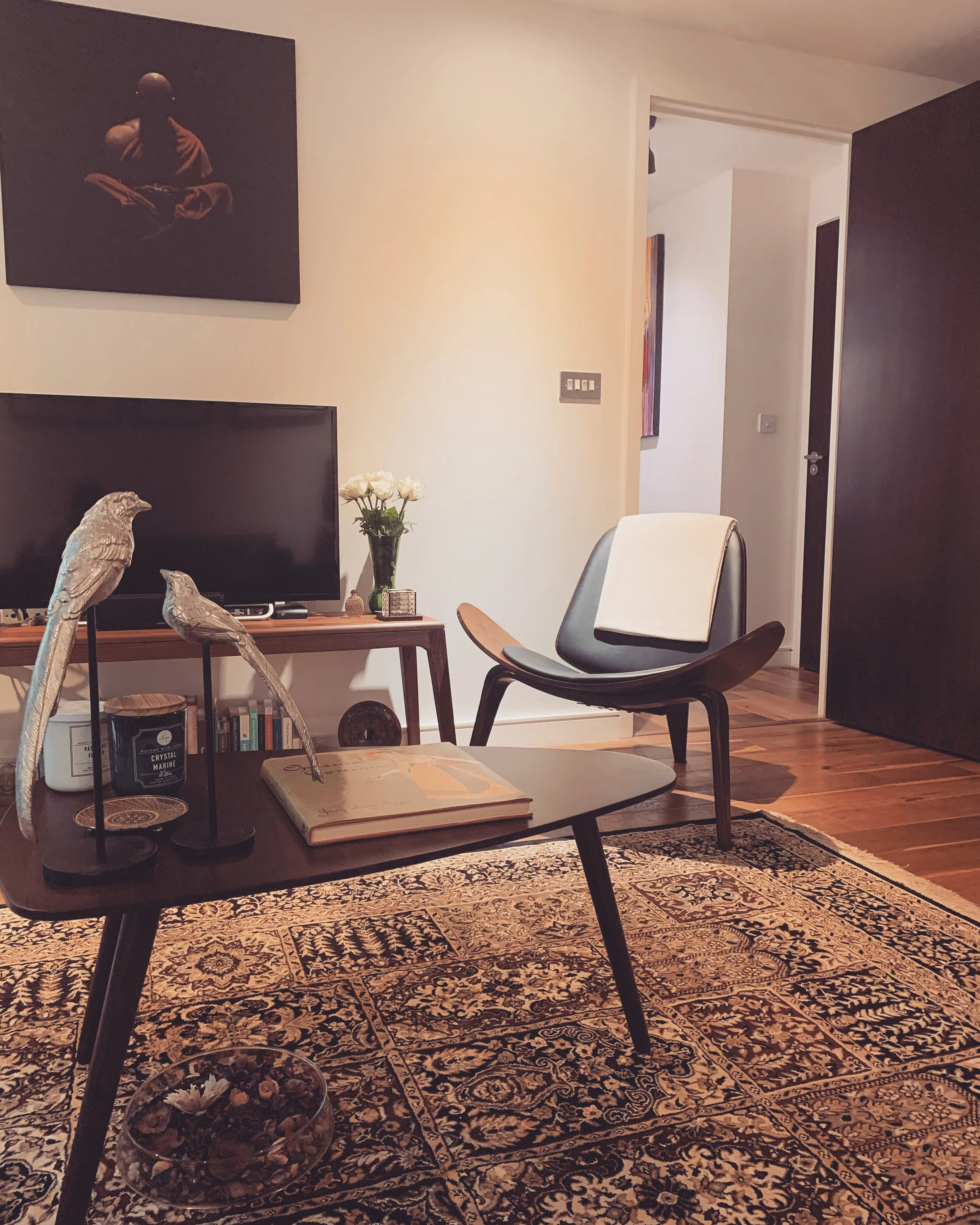 Small London living room with a large patterned Persian-style rug, plain black leather chair, and solid walnut furniture — an example of one dominant pattern balanced by solid colours.