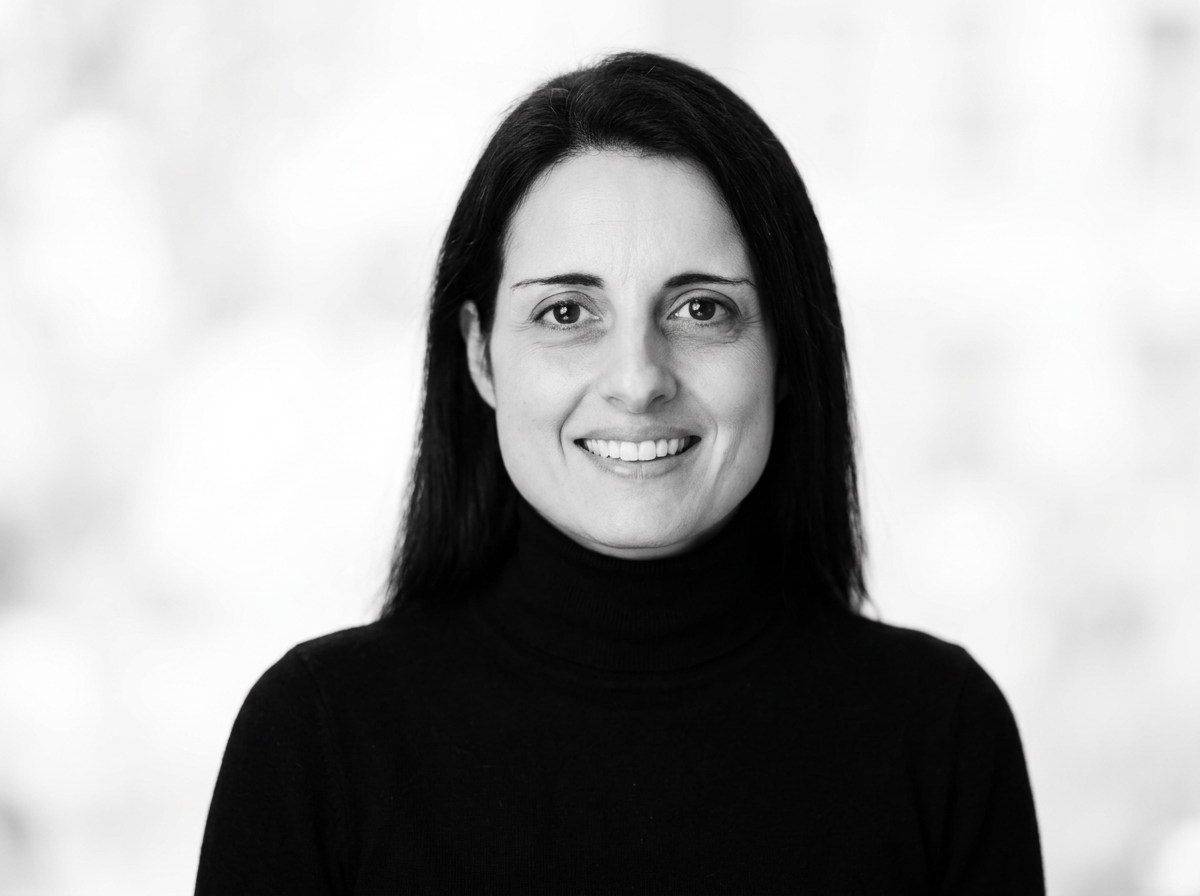 Black and white portrait of a woman with long dark hair, smiling, wearing a black turtleneck.