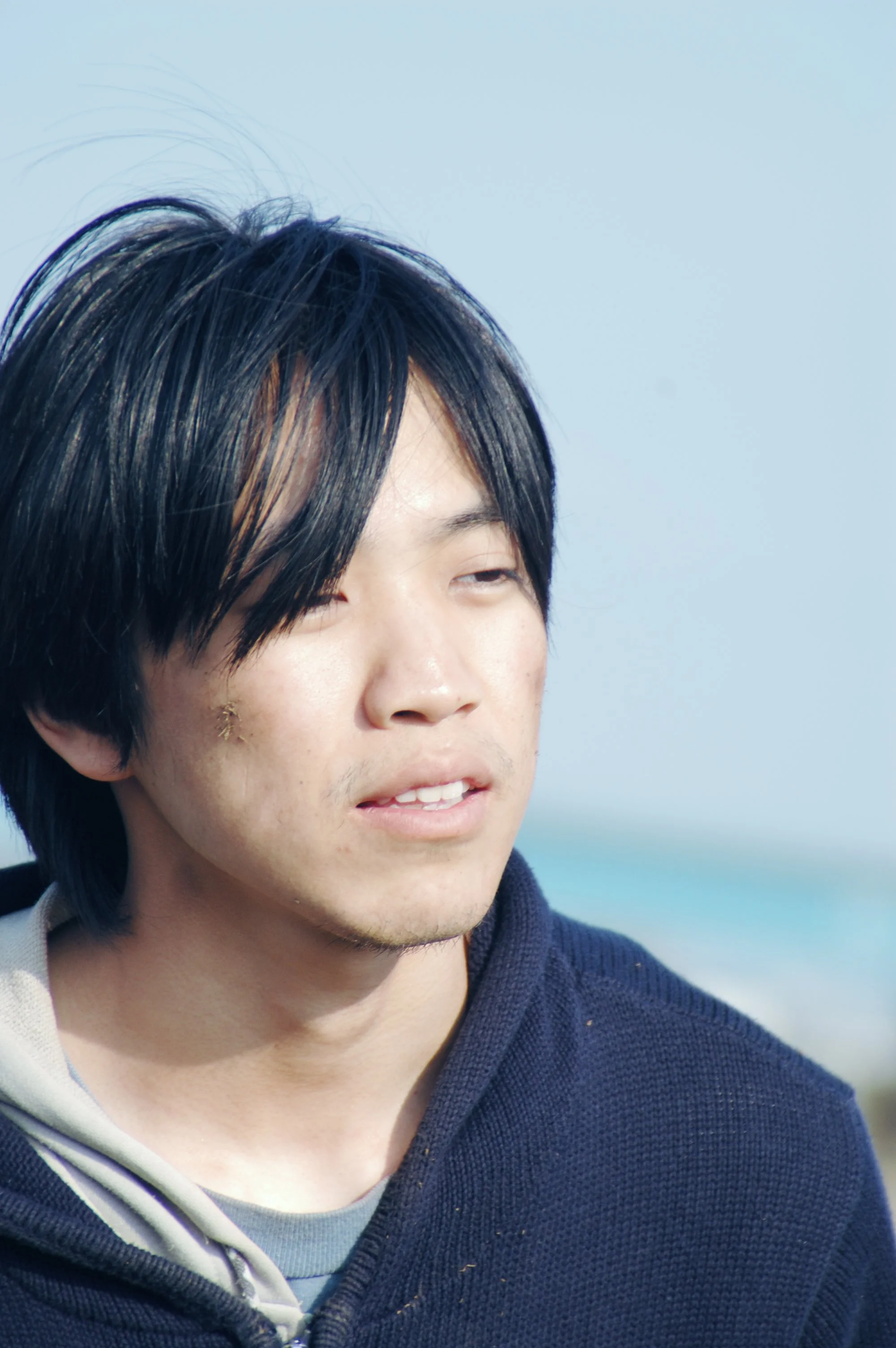 海辺で若い男性が微笑みながら遠くを見ている風景