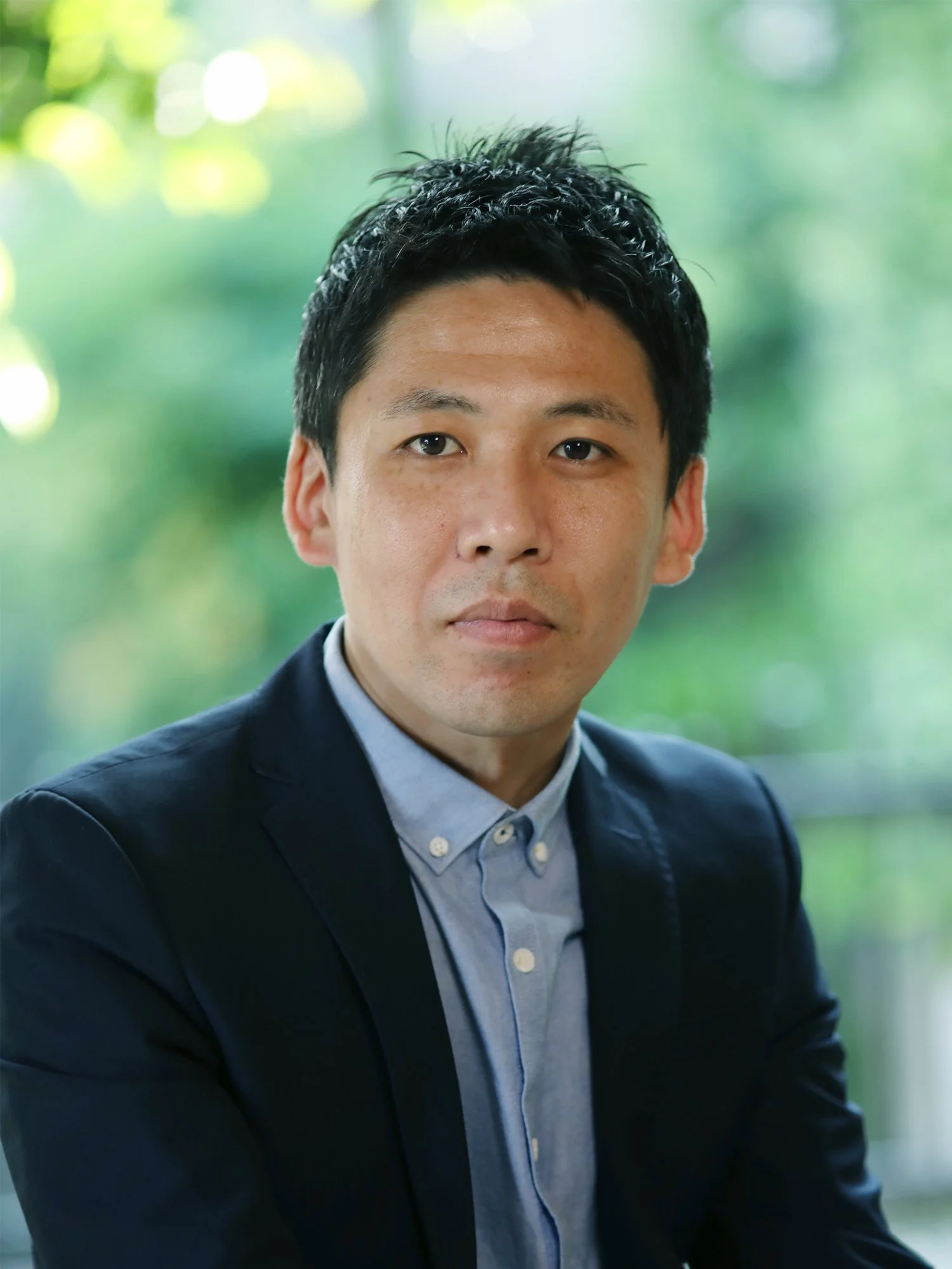 ビジネスマン風の男性が正面を見ている。背景は緑色の自然の景色。