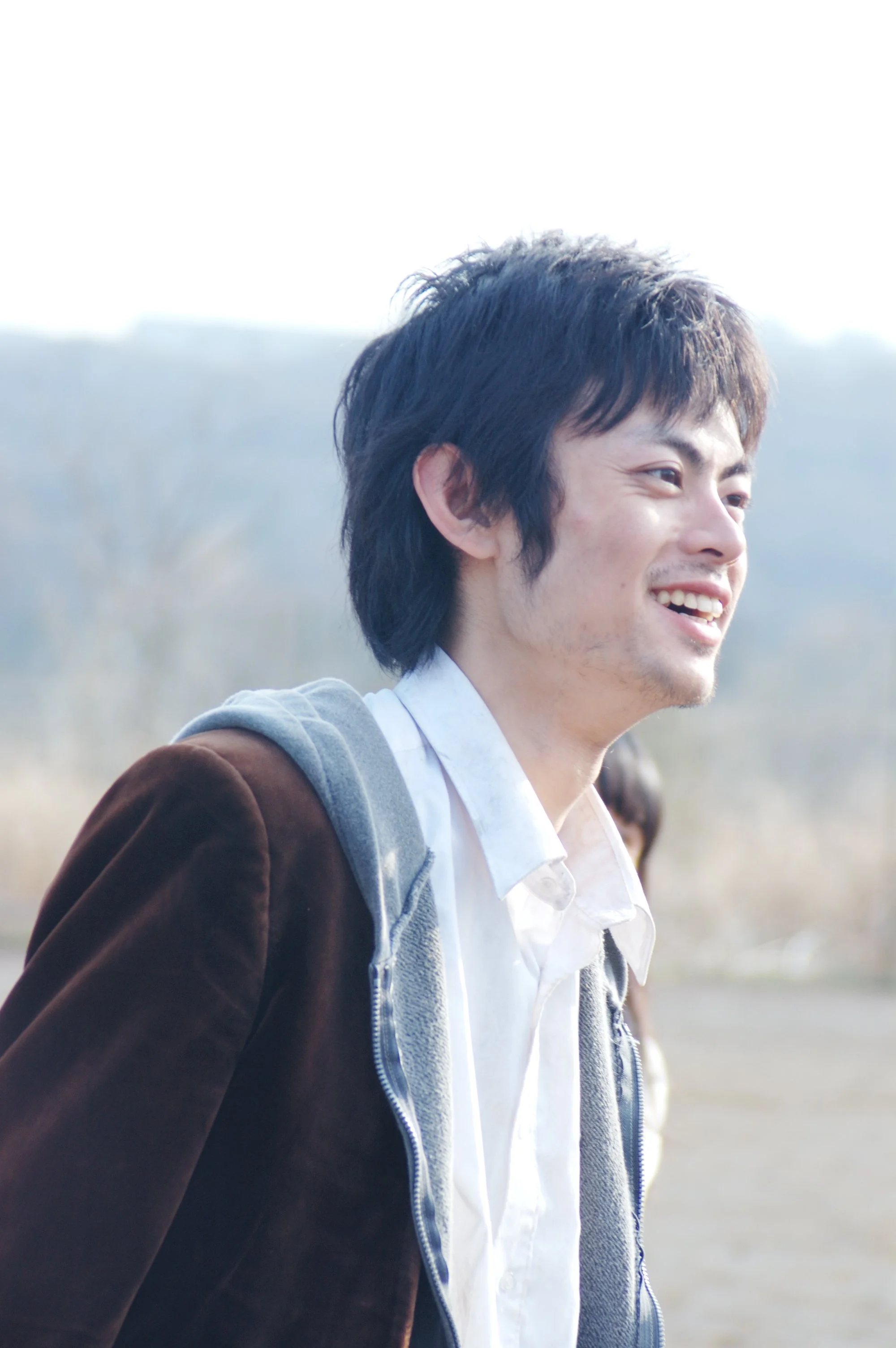 笑っている若い男性の横顔の写真。背景は自然の風景。