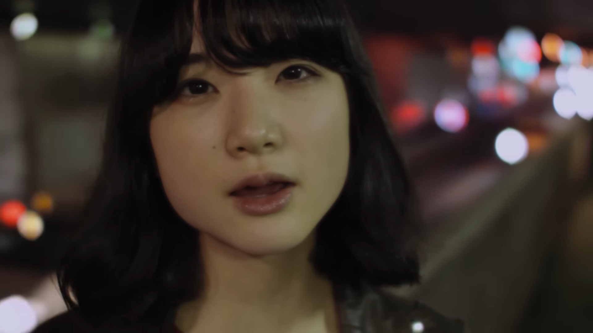 夜の街を背景に、黒髪の女性の顔がアップで映っている