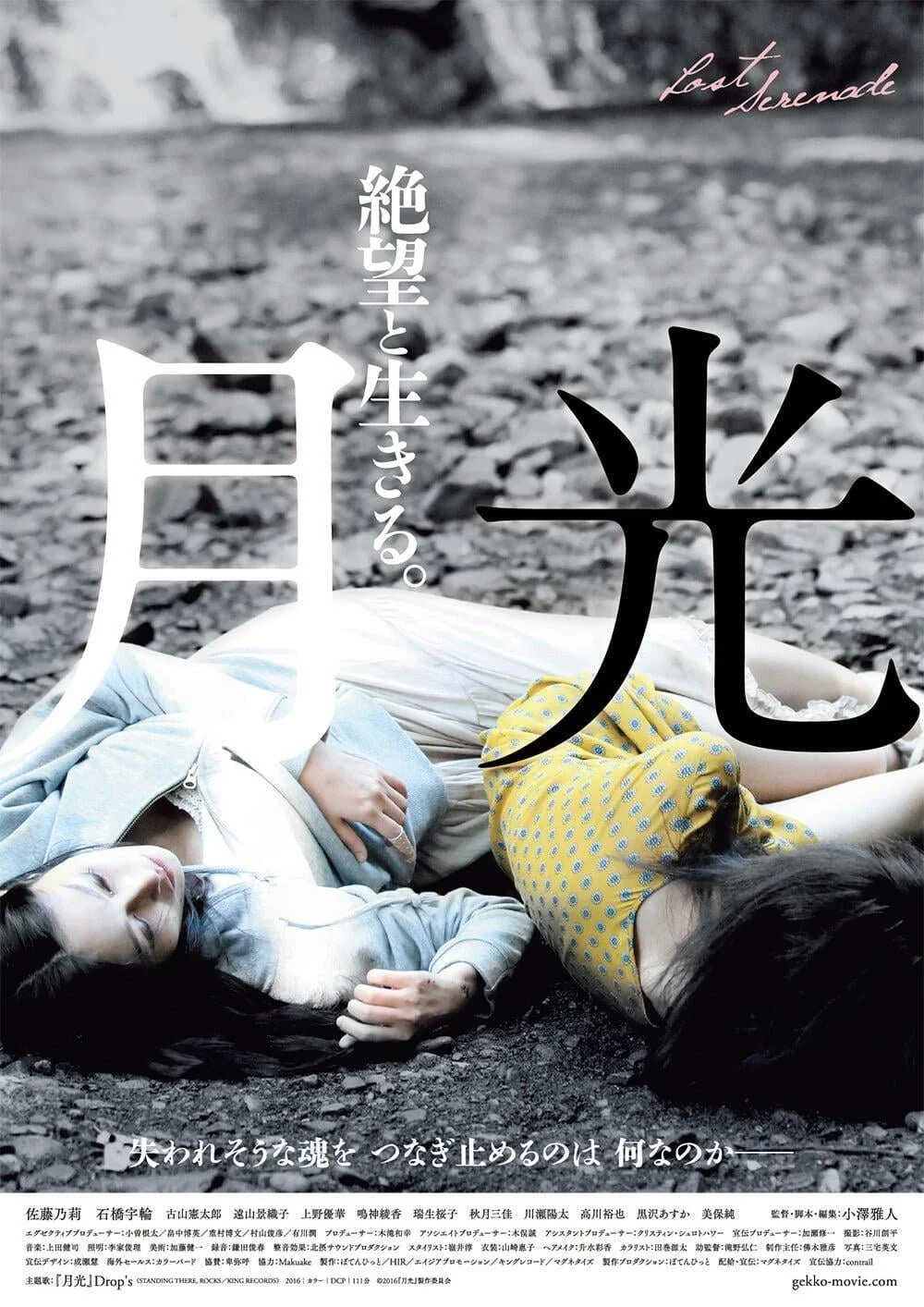 二人の若い女性が岩や土の上に横たわっている。1人は白と青の服を着ていて目を閉じている。もう1人は黄色のドット柄の服を着ている。背景は岩の荒地。