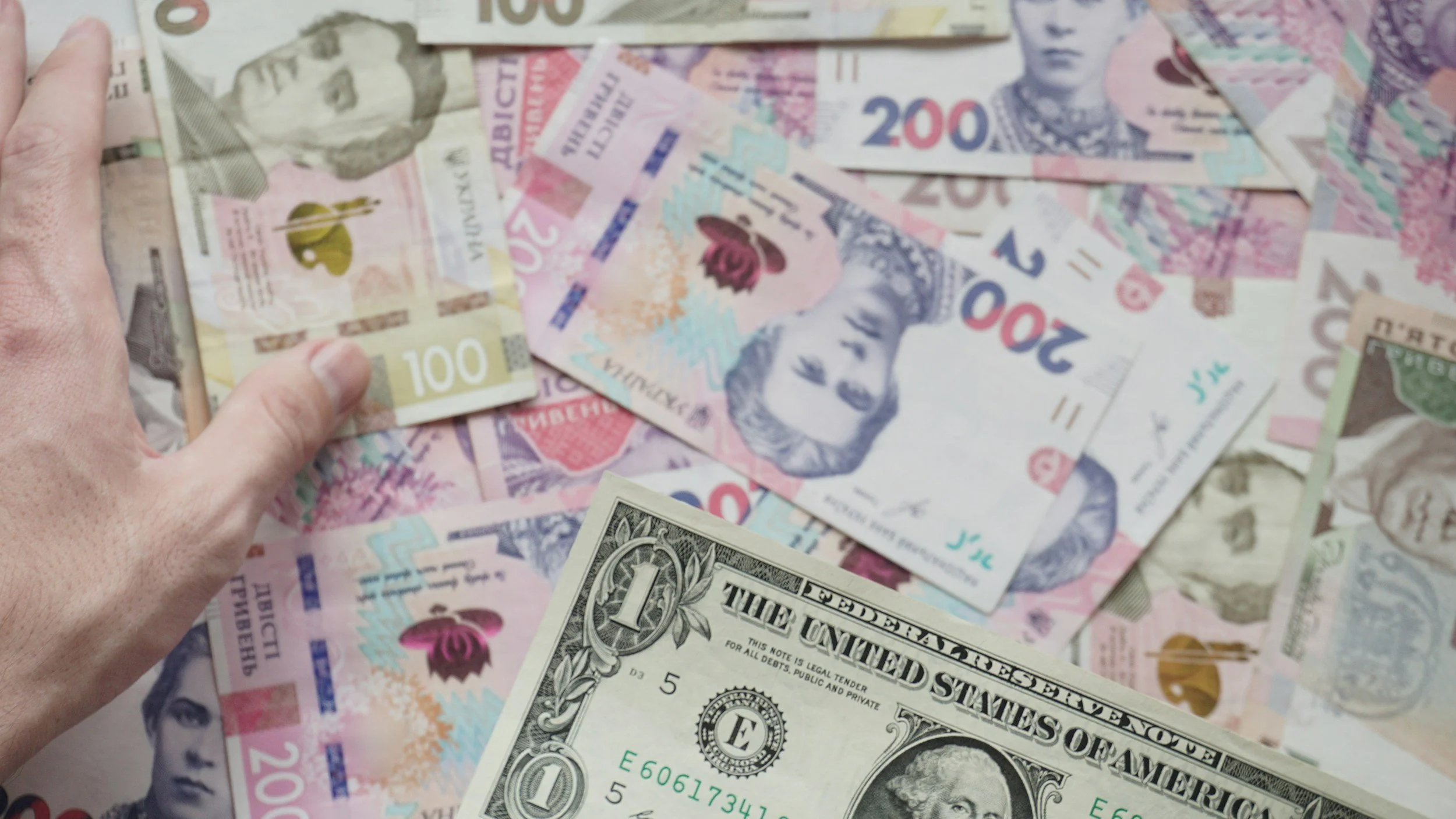 Canadian and U.S. dollar bills scattered on a surface, with a hand holding a 100 Canadian dollar bill.