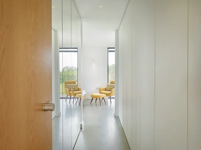 View of a modern interior room with yellow chairs and large windows with a view of trees outside.