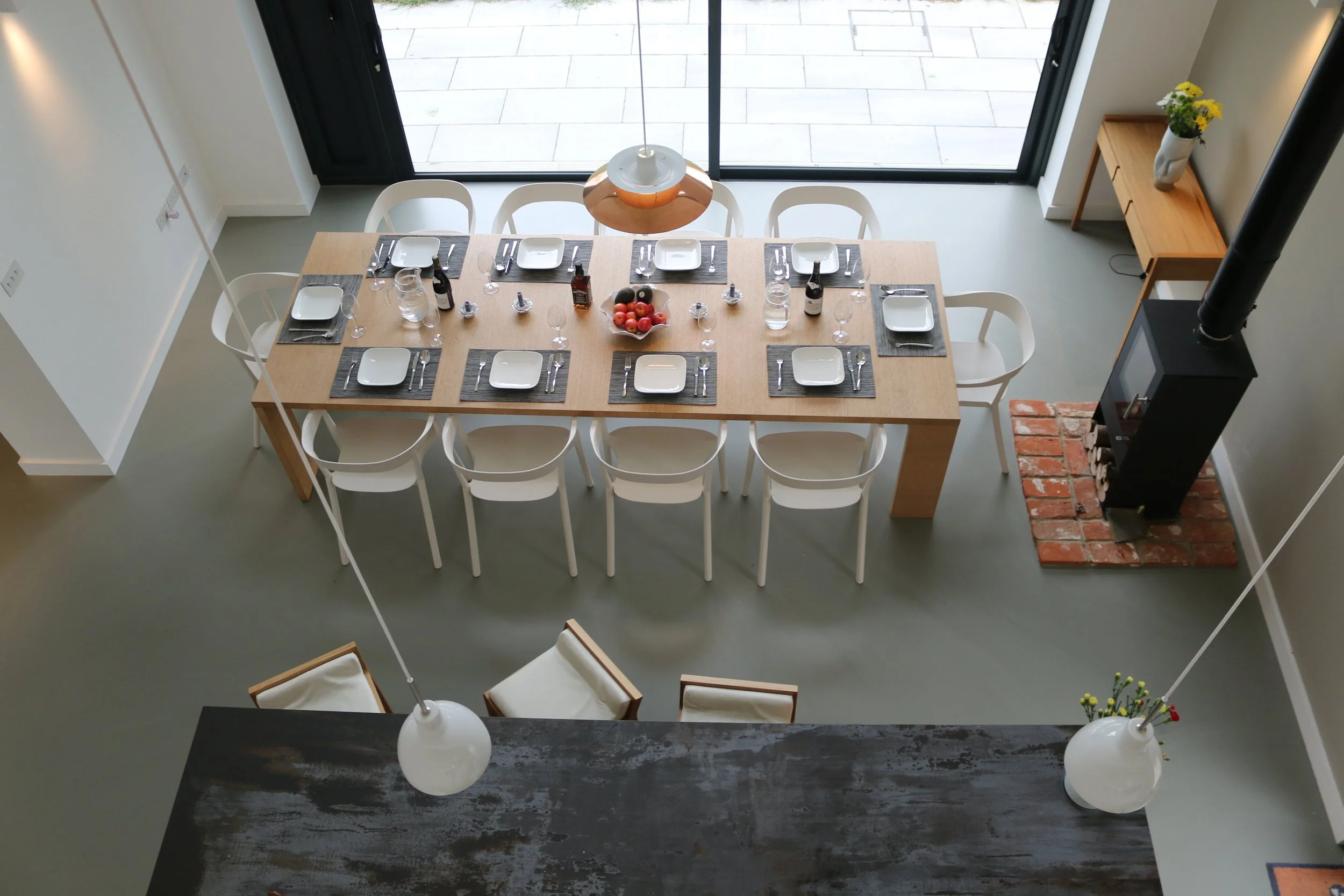 A dining table set for six with plates, silverware, glasses, bottles, and a bowl of fruit, located near a large sliding glass door with a view of an outdoor patio, in a modern kitchen or dining area.
