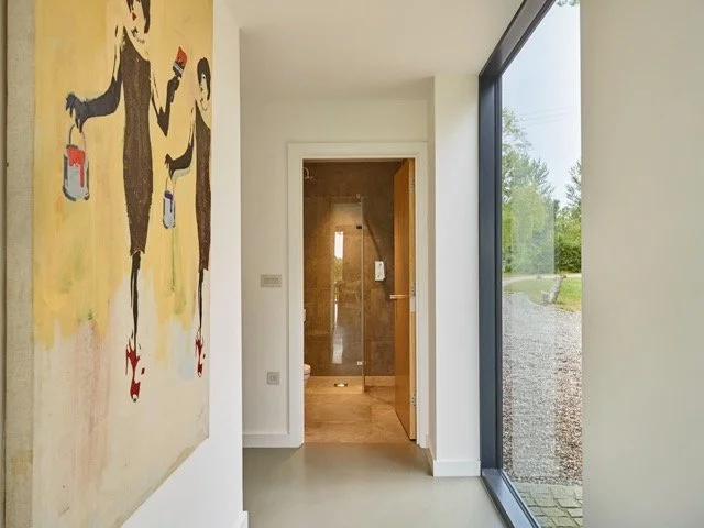 Modern interior hallway with a large abstract painting on the left, a glass wall on the right, and a door leading to a bathroom in the background.