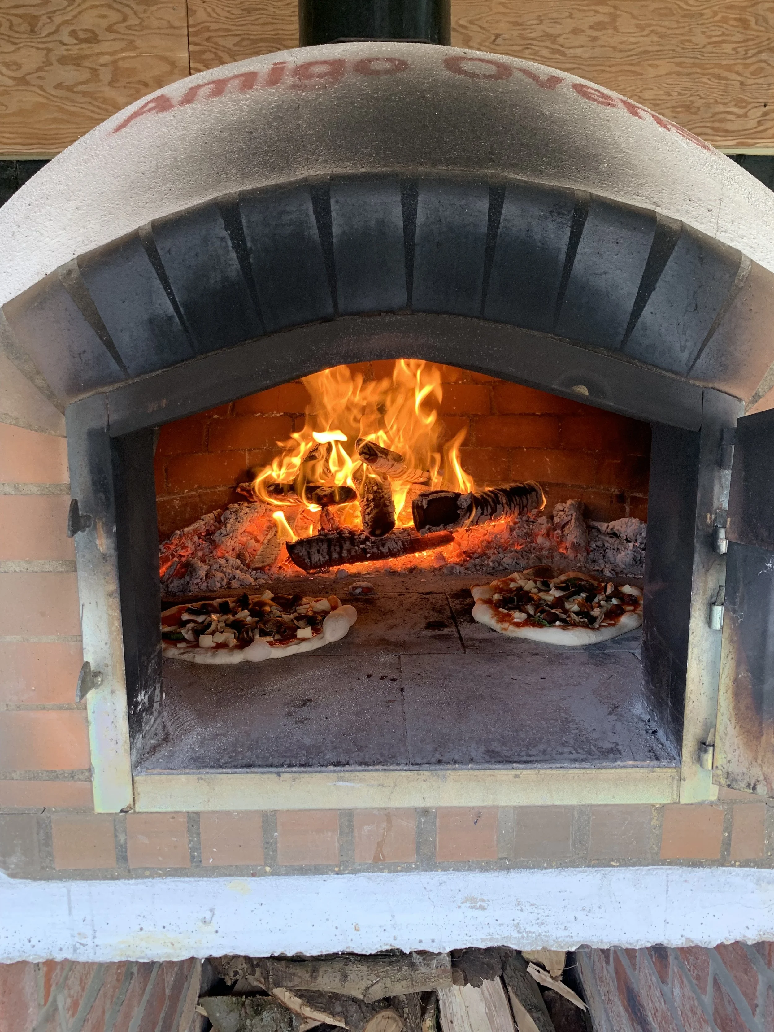 A brick pizza oven with two small pizzas cooking inside and flames in the background.