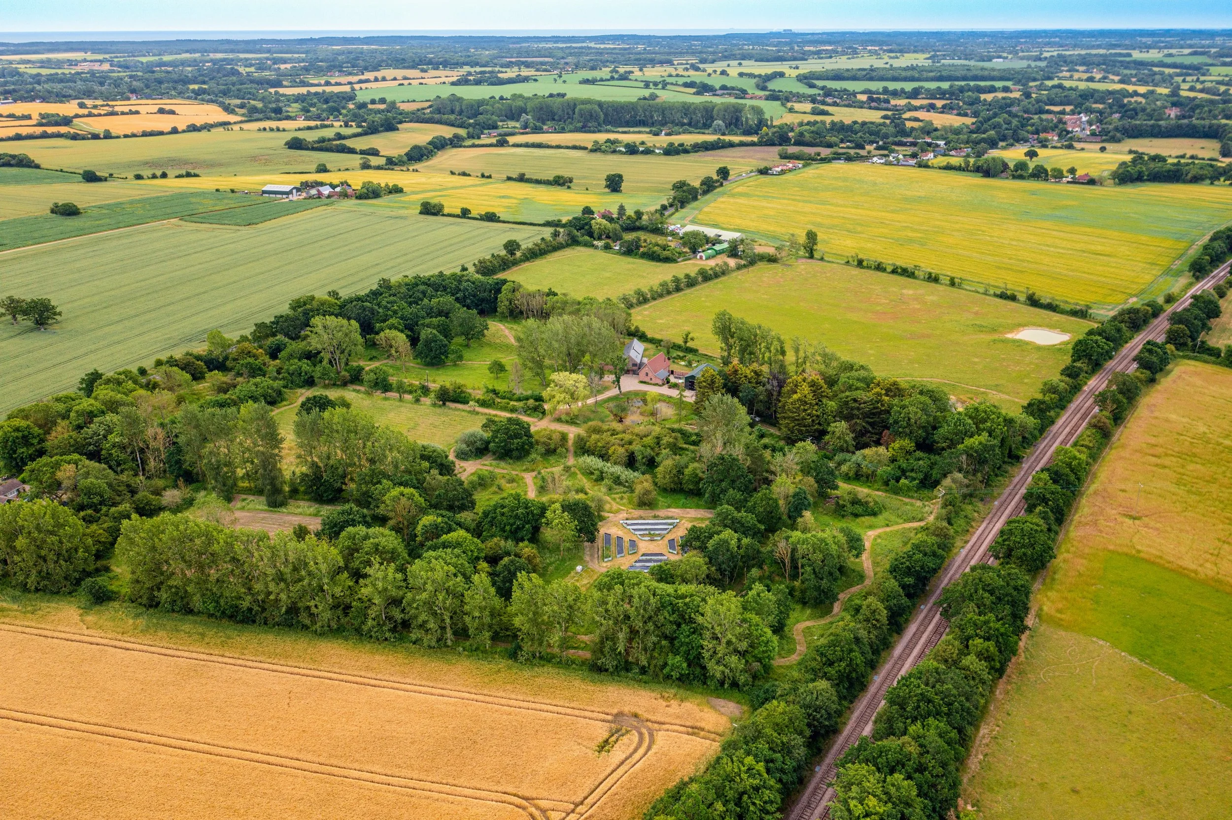 Aerial view of a rural landscape with farmland, green trees, houses, and a railroad track running through the fields.