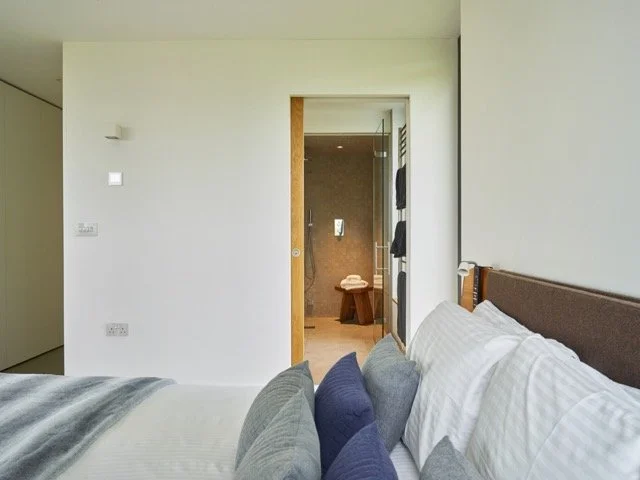 A view of a bedroom with a bed and pillows, and an open door leading to a bathroom with a towel on a stool.