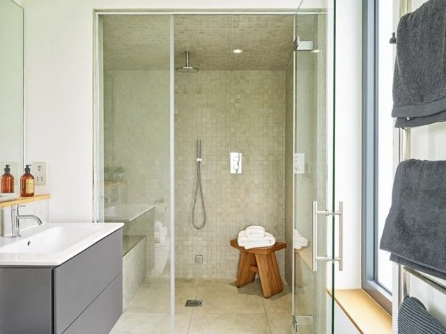 Modern bathroom with a glass-enclosed shower area, a dark vanity with a sink, and towels on a heated rack next to a large window.