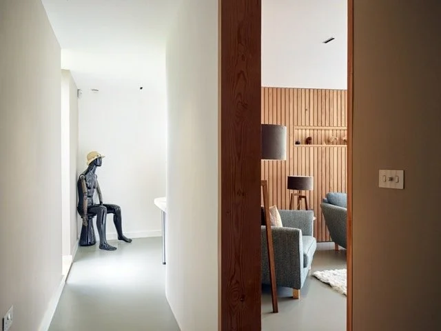 A view of a modern living room through an open doorway, with a cozy seating area, wooden walls, and contemporary decor.