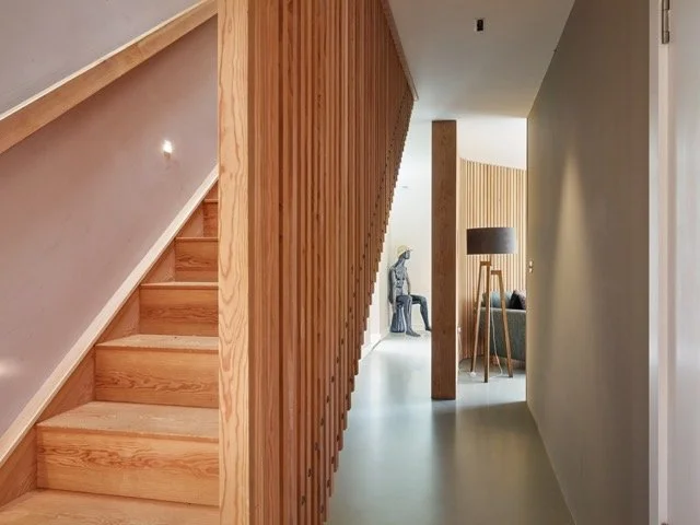 Interior view of a modern home with wooden stairs, a decorative statue, a floor lamp, and a gray living room.