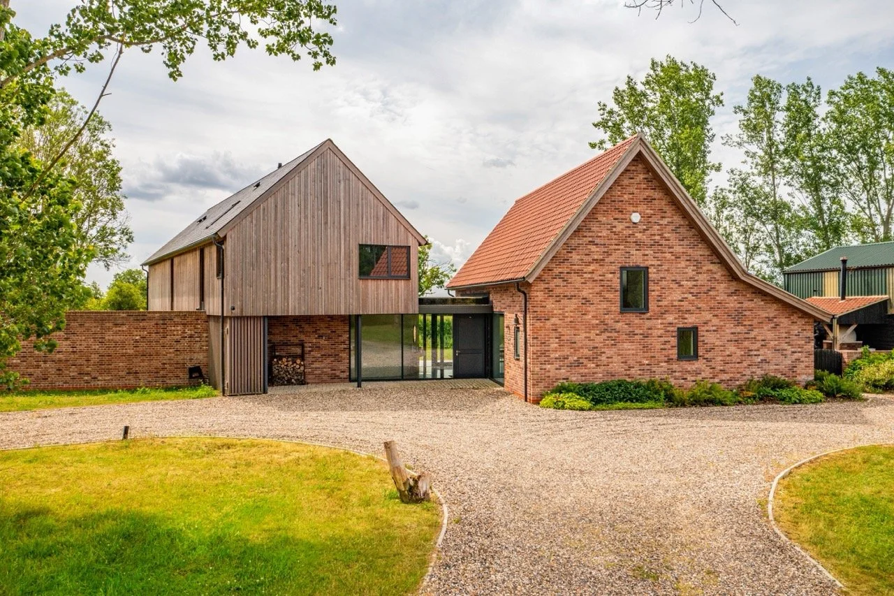 A modern residential home combining brick and wood siding, with a gravel driveway and green lawn in a rural setting.