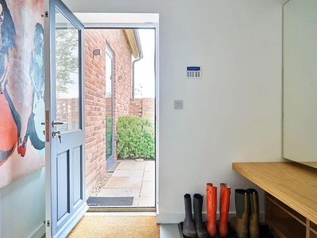 Open door leading outside to a pathway with bushes and brick house wall visible.