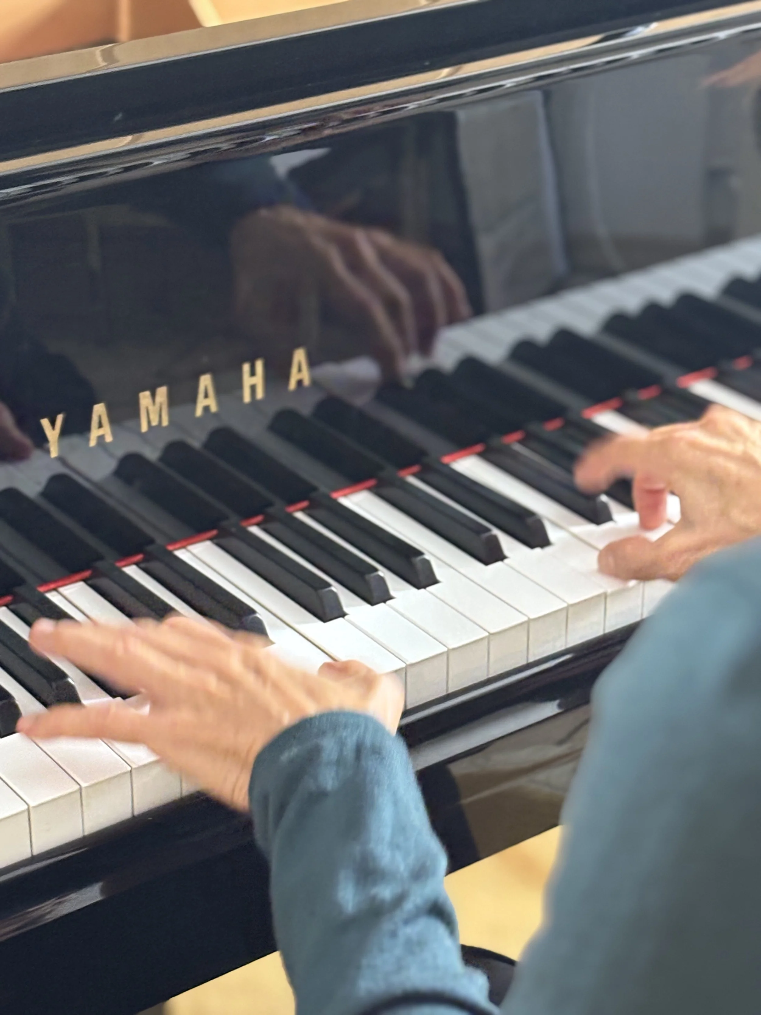 Nahaufnahme eines Menschen, der auf einer schwarzen Yamaha Klavier spielt, mit Schwerpunkt auf den Tastaturbereich.