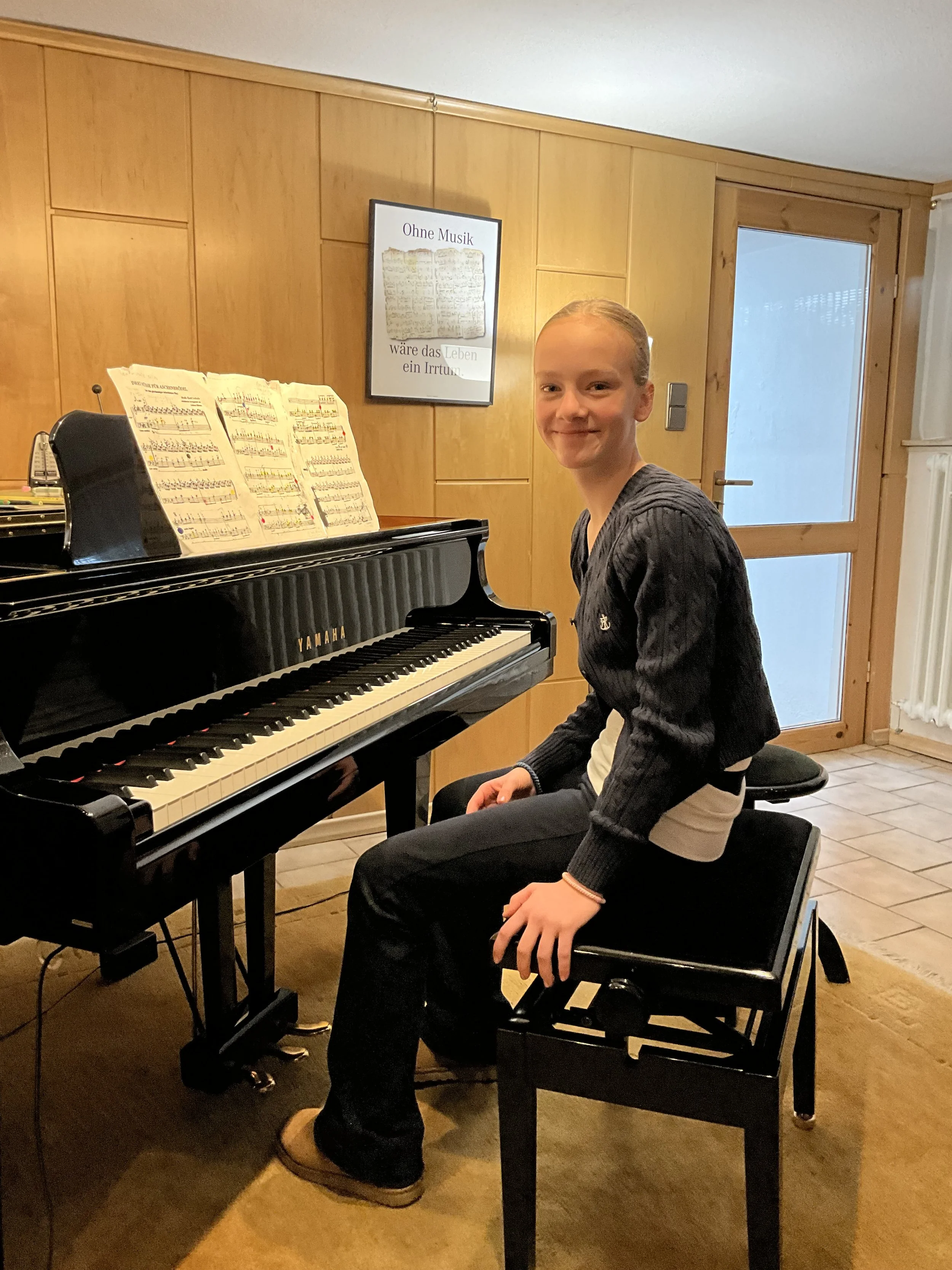 Junge Frau sitzt an einem schwarzen Yamaha Klavier im Raum, spielt Klavier und lächelt in die Kamera.