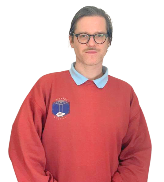 A man with glasses and facial hair wearing a red sweater with a blue collar and a logo on the chest, standing against a plain background.