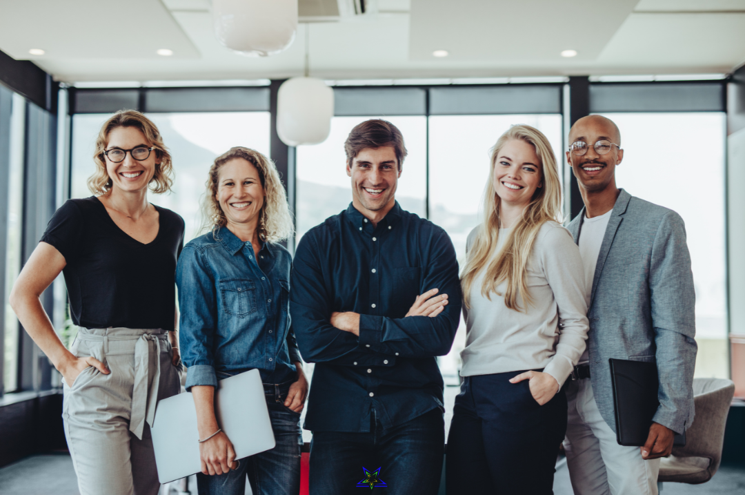 Five emerging leaders wearing casual dress are standing in a line and smiling at the camera. They look relaxed and two are holding laptops. They're in an office with big windows and the room is light and airy