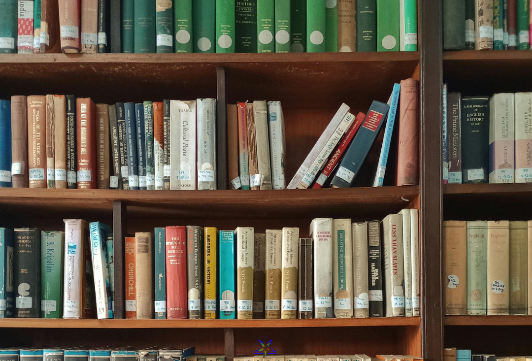 Image shows a set of wooden library shelves filled with differently coloured books