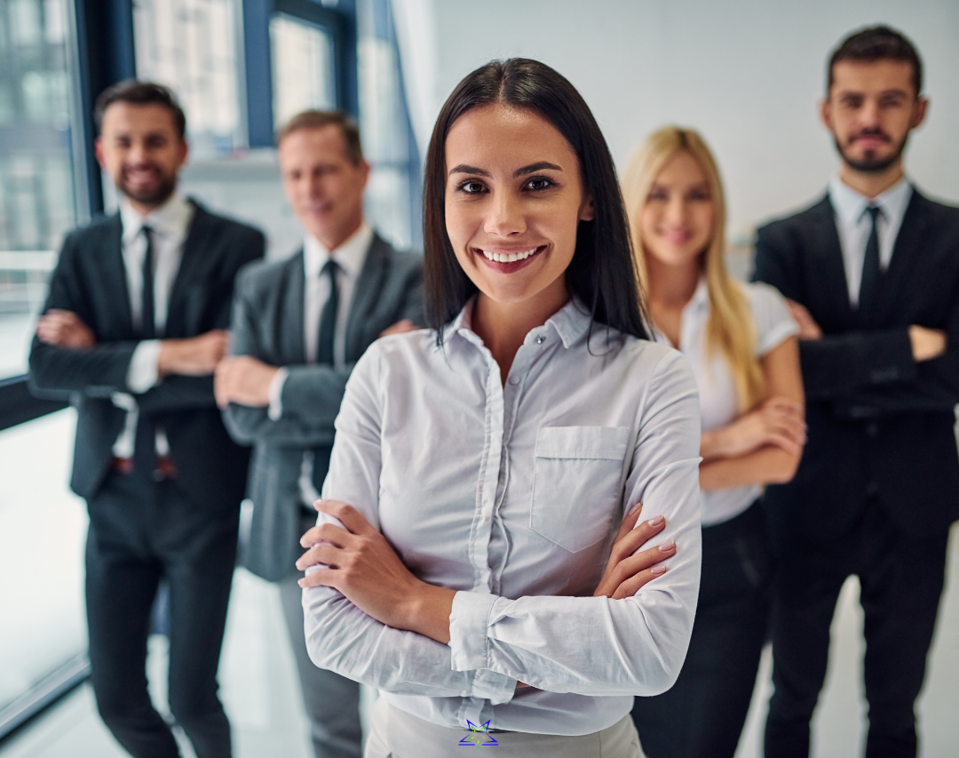 Image shows a group of five smiling office workers, three men and two women. They're stood with their arms crossed, facing the camera and smiling