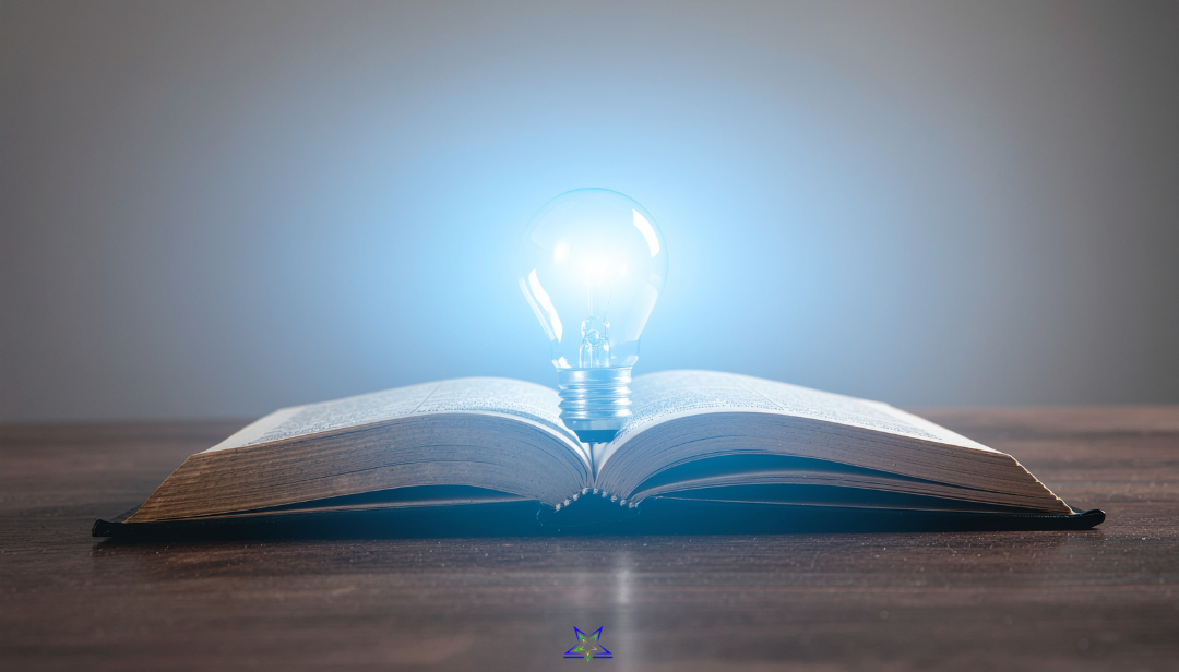 Image shows a hardback book lying open on a wooden table. In the middle of the book, over the spine, sits and illuminated lightbulb