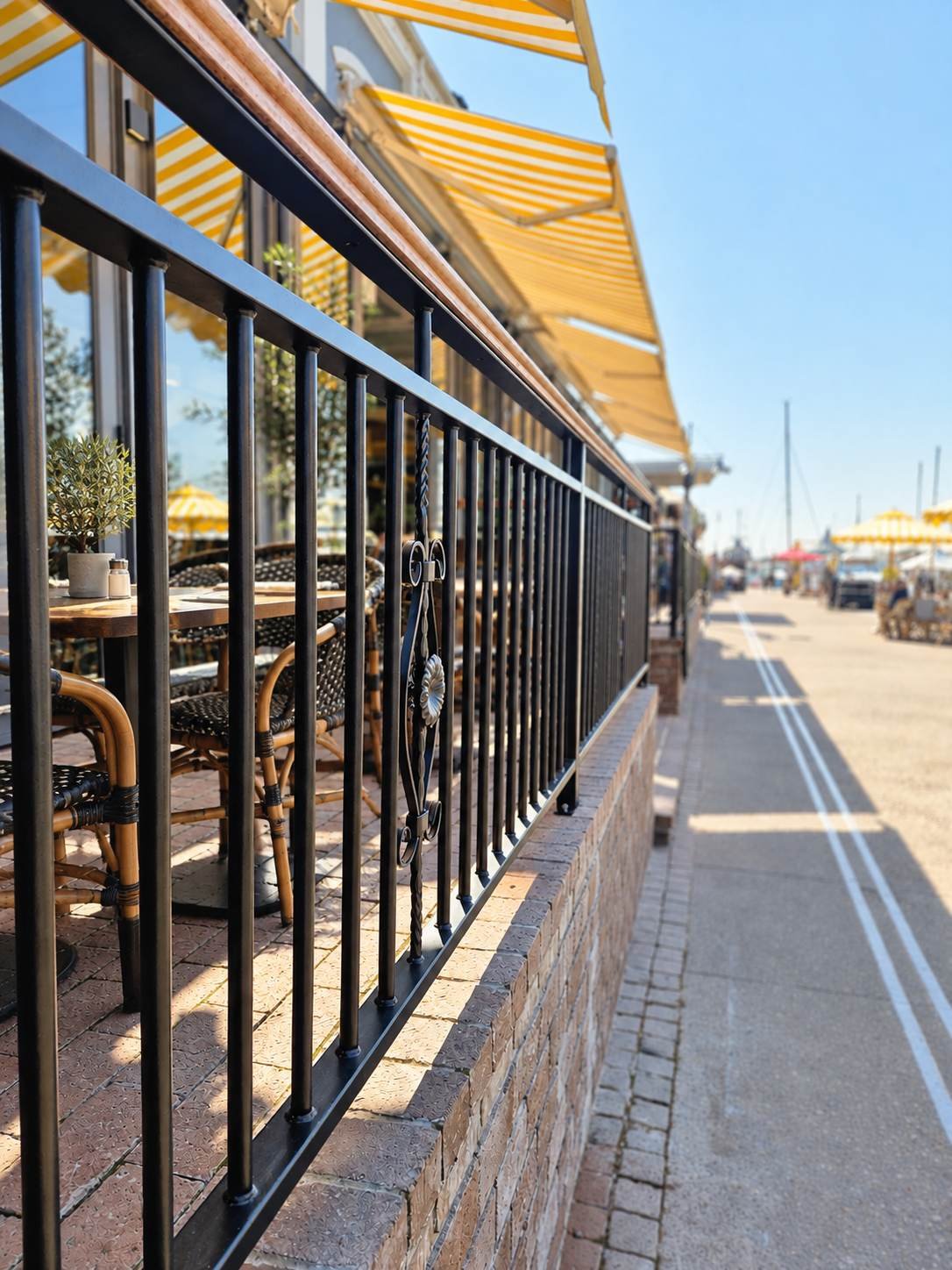 Black powder-coated steel balustrade with a timber handrail and a decorative scroll detail, installed on a brick wall at a restaurant at the V&A Waterfront