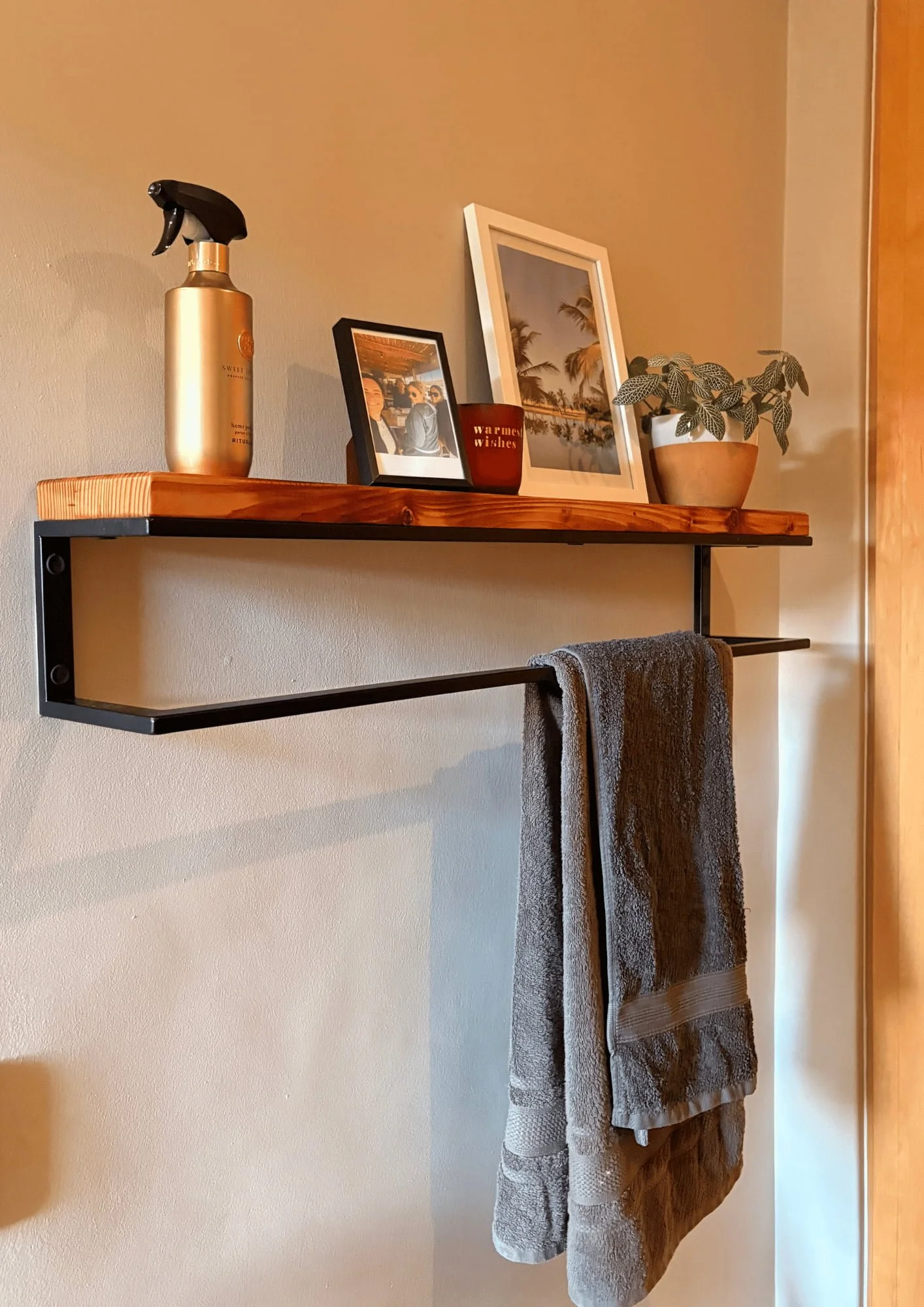 A Bathroom Shelf with pictures and a plant on top of it and a towel hanging from its steel bar below.