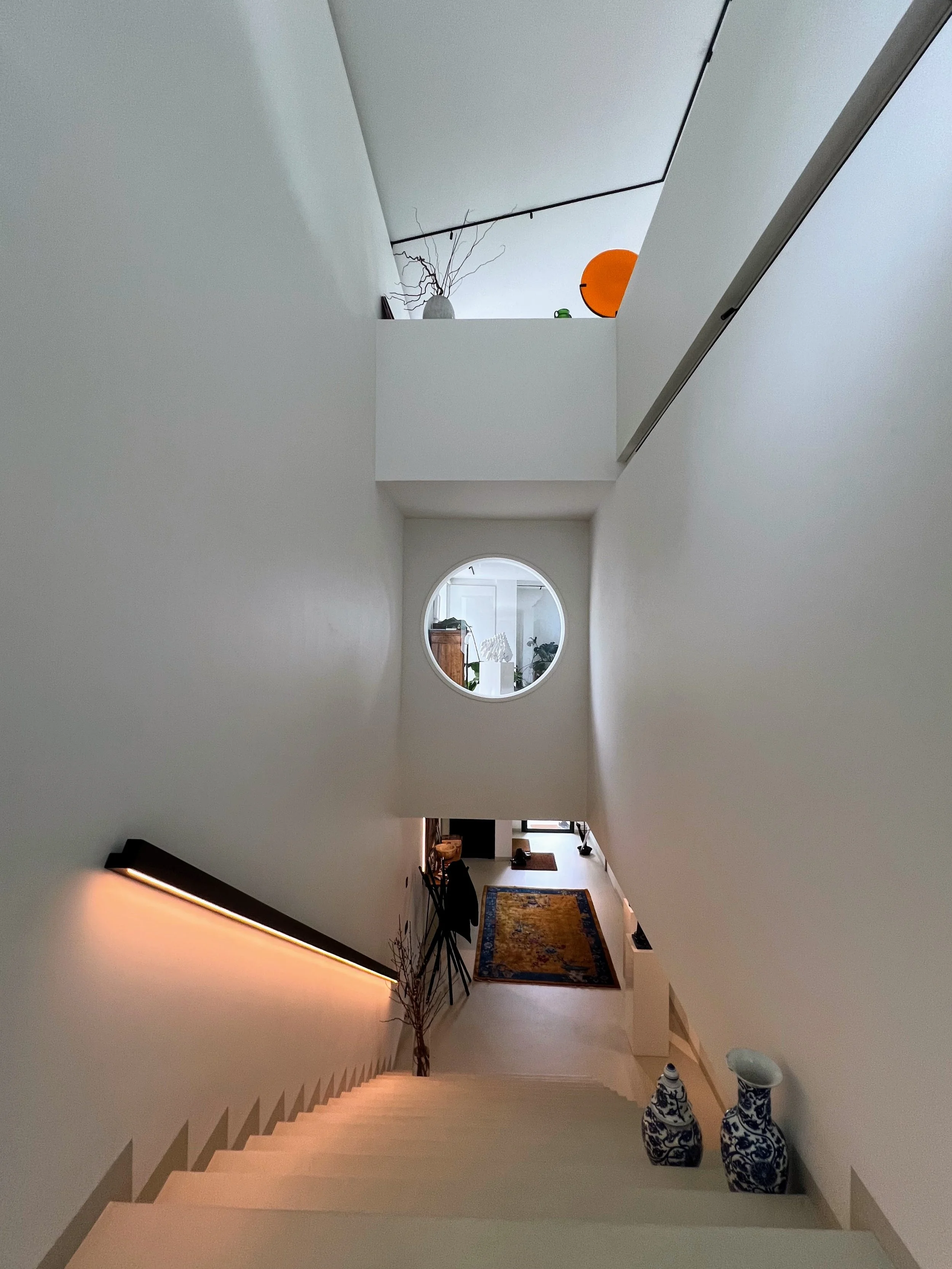 Vista dall'alto di un interno moderno con scale, pareti bianche, decorazioni e apertura rotonda in una parete