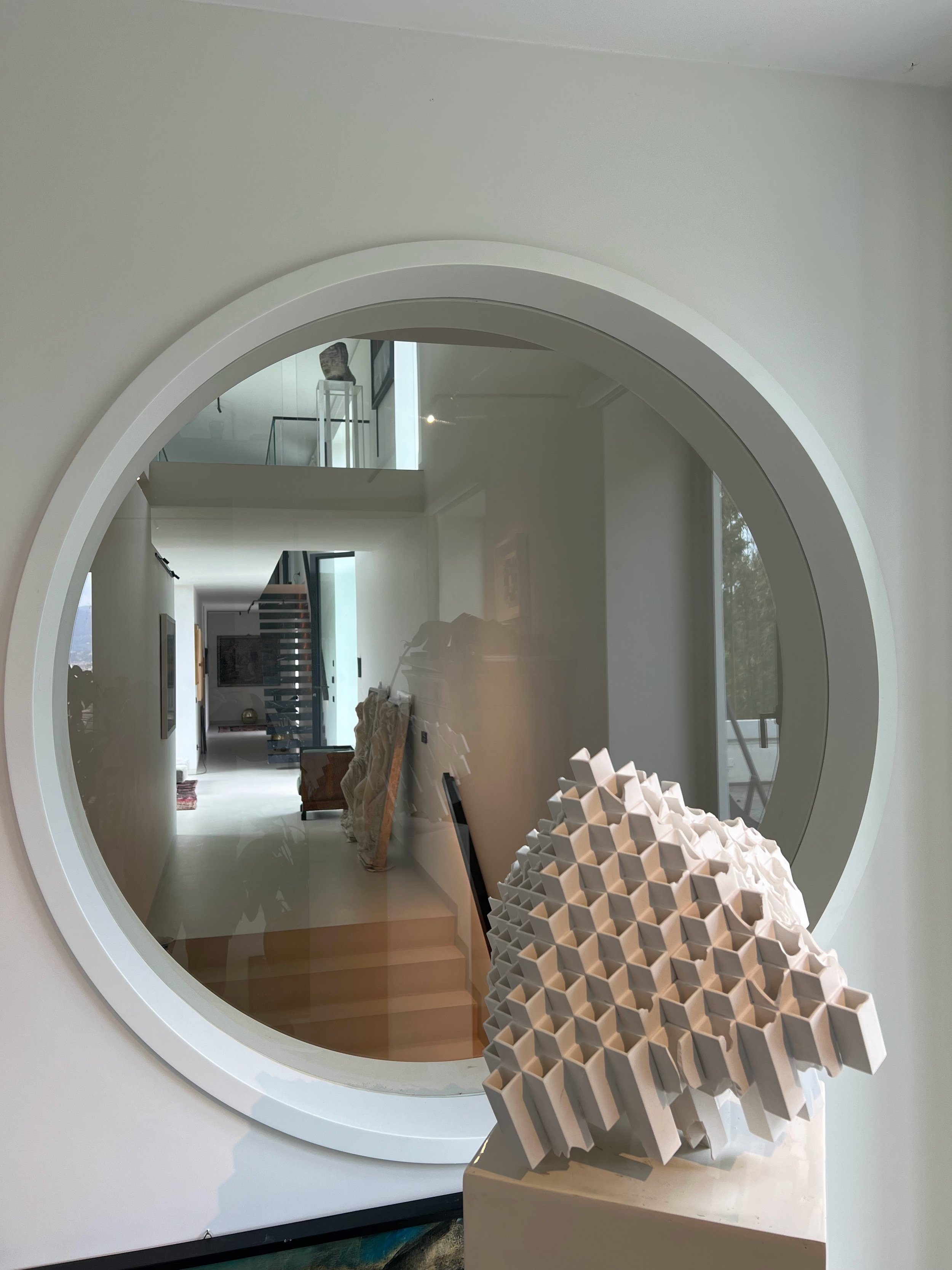 Finestra rotonda in una parete bianca che riflette l'interno di una casa moderna, con oggetti d'arte e arredi.