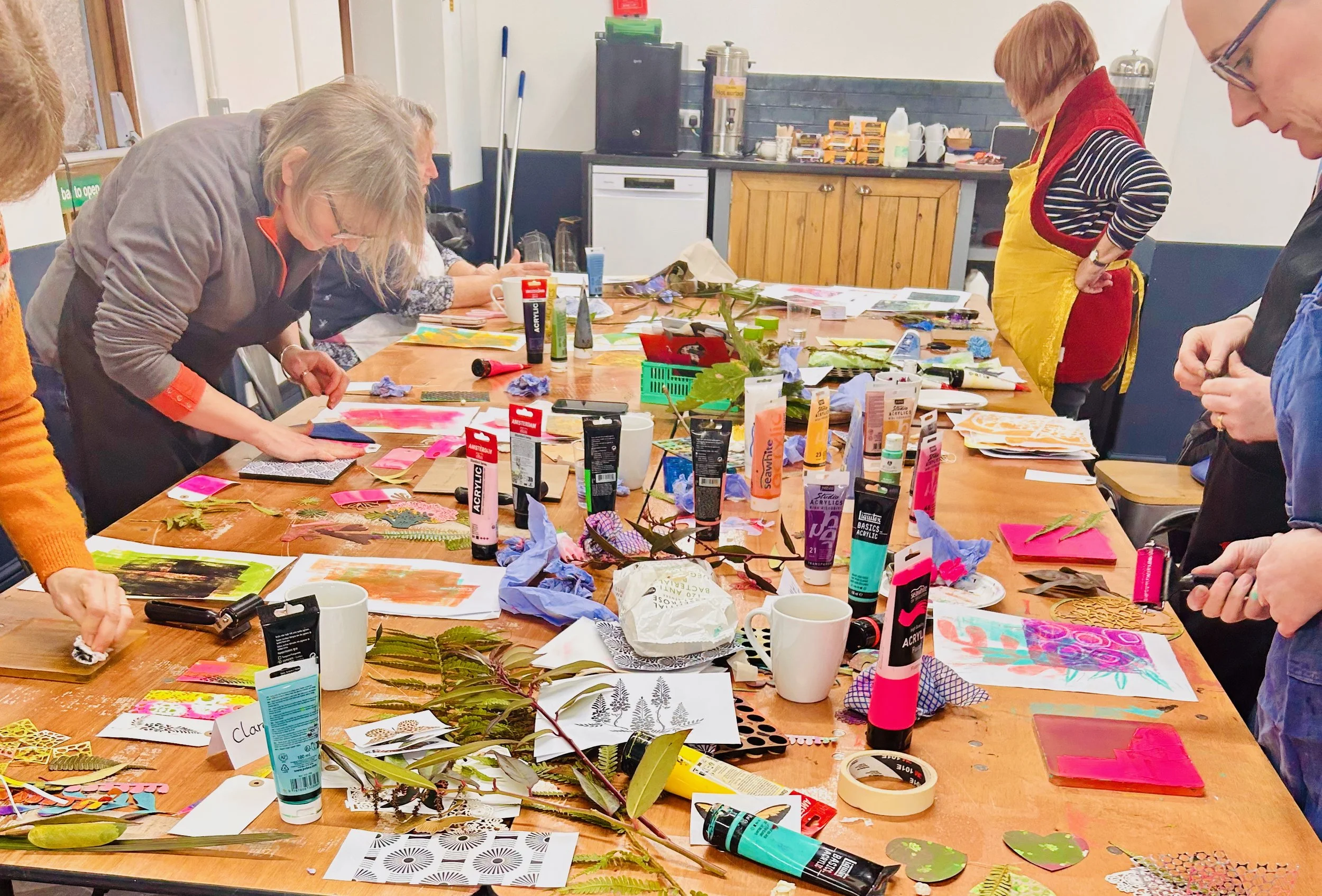 Participants gathered around table creating colourful mono-prints during a One More Print Gelli printing workshop in Horsham Wes Sussex.