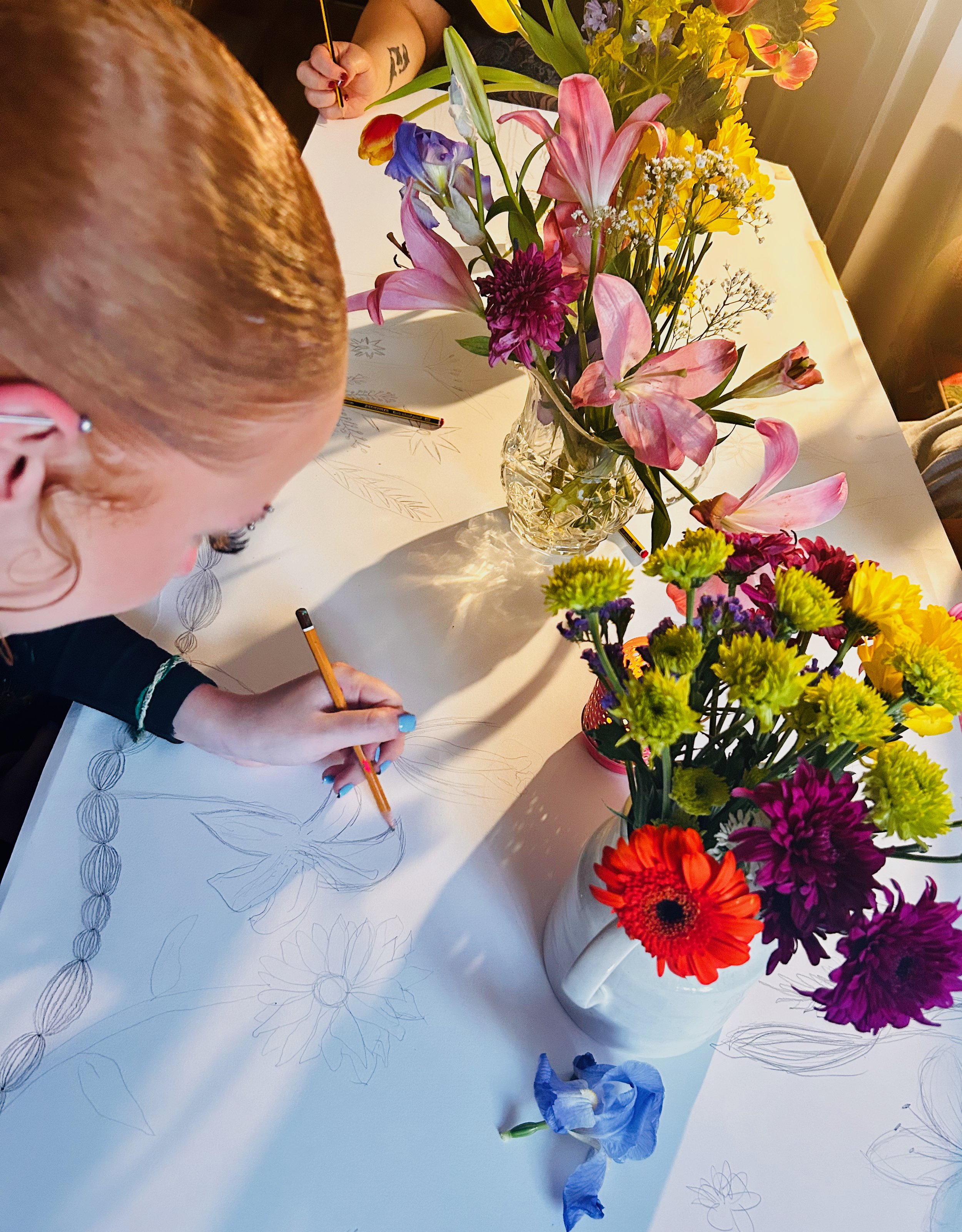 Participant using pencil to draw flowers in vase on a large piece of paper.