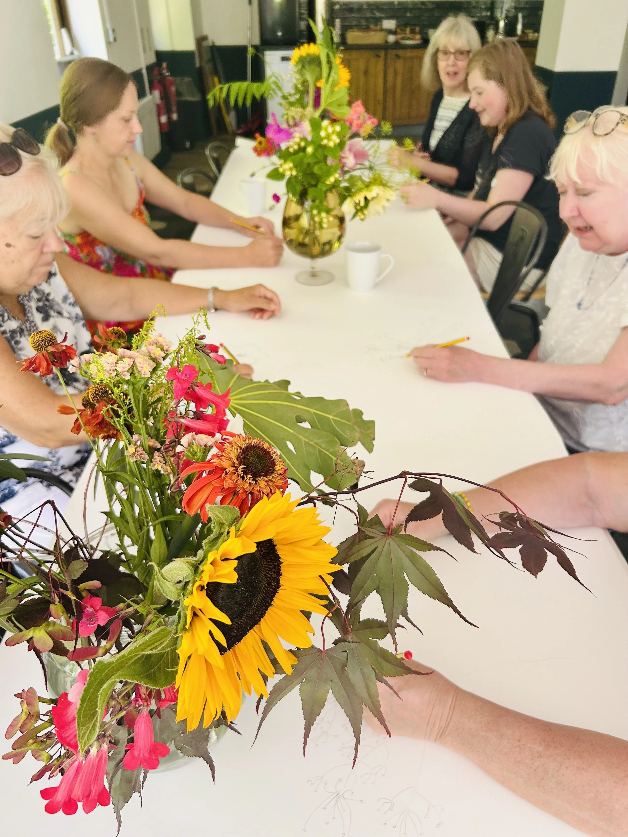 Creative workshop in Horsham West Sussex participants gathering around a shared table filled with flowers and art materials.