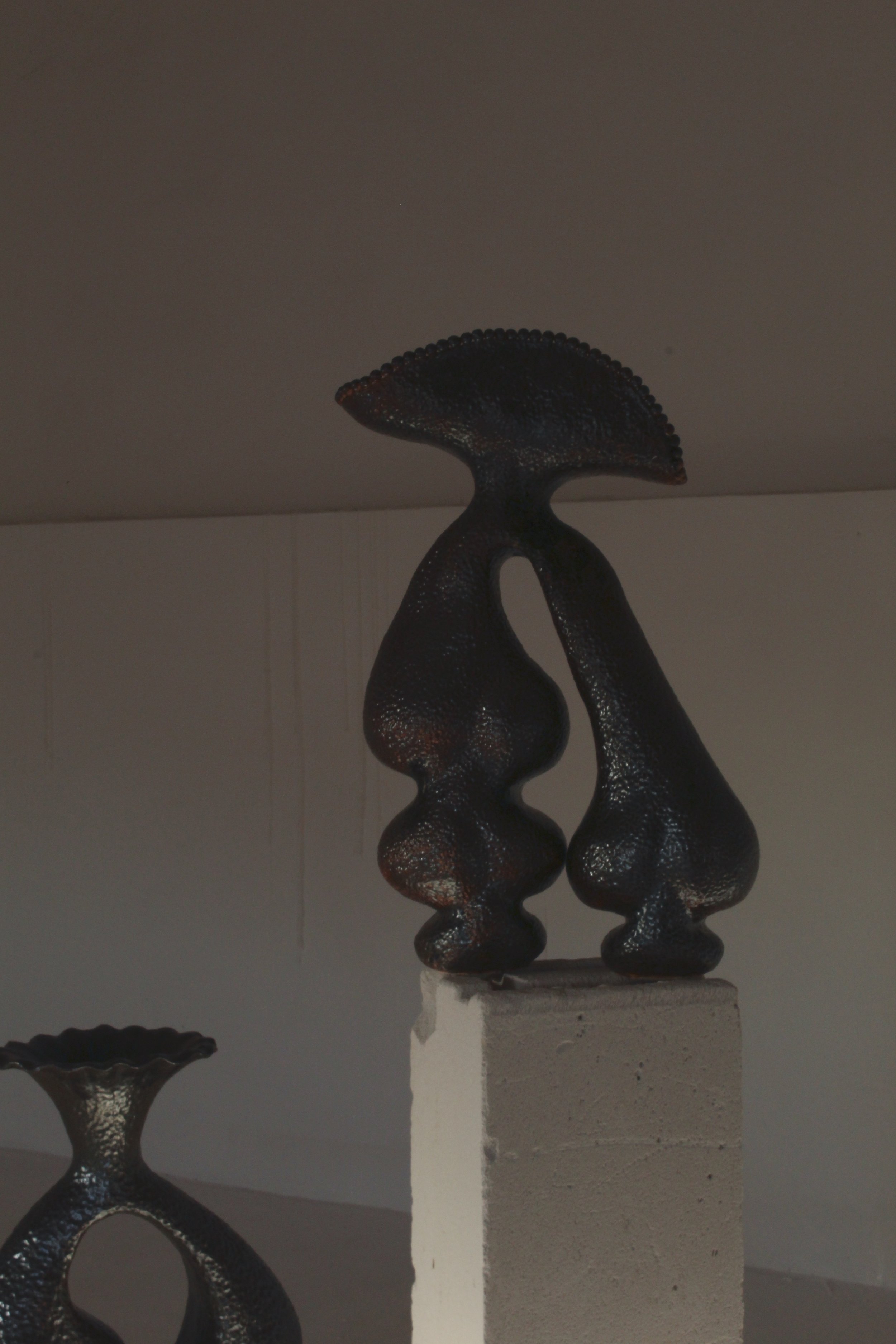 Black abstract sculpture on a white pedestal in an art gallery.