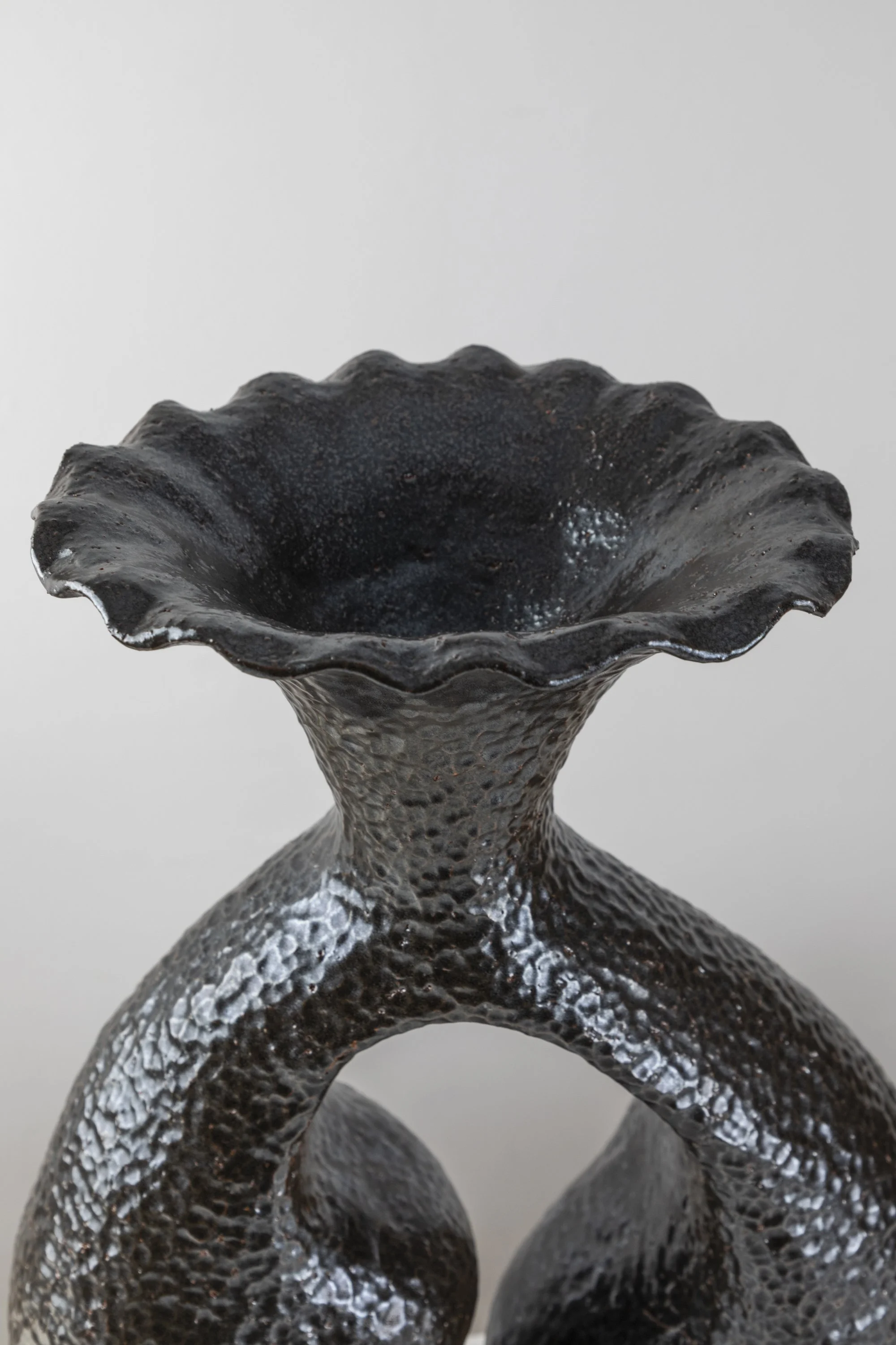 Close-up of a black textured ceramic sculpture with a wide, wavy top and two intertwined loops at the base.