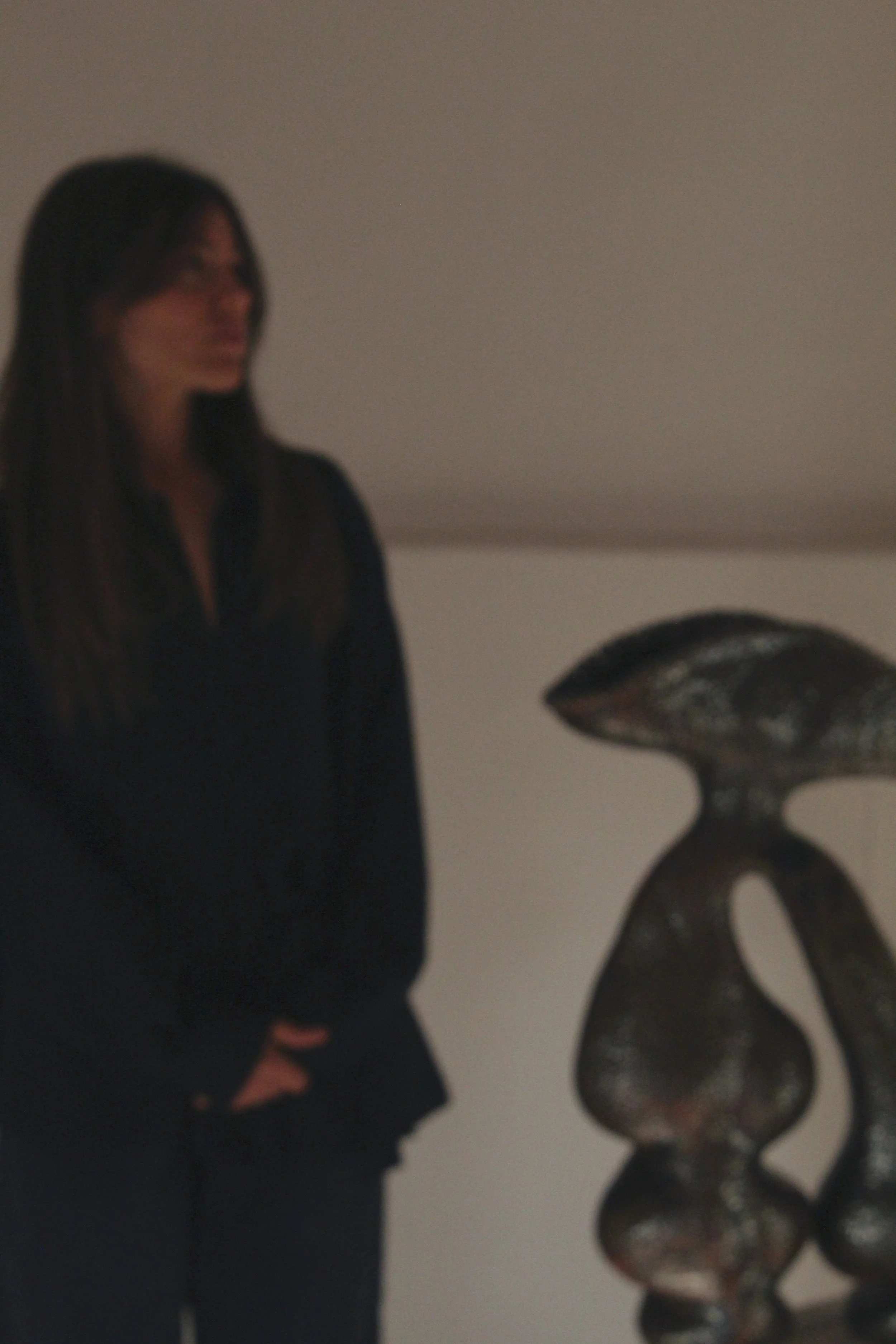 A woman with long dark hair standing near a large abstract metal sculpture in an art gallery or museum.