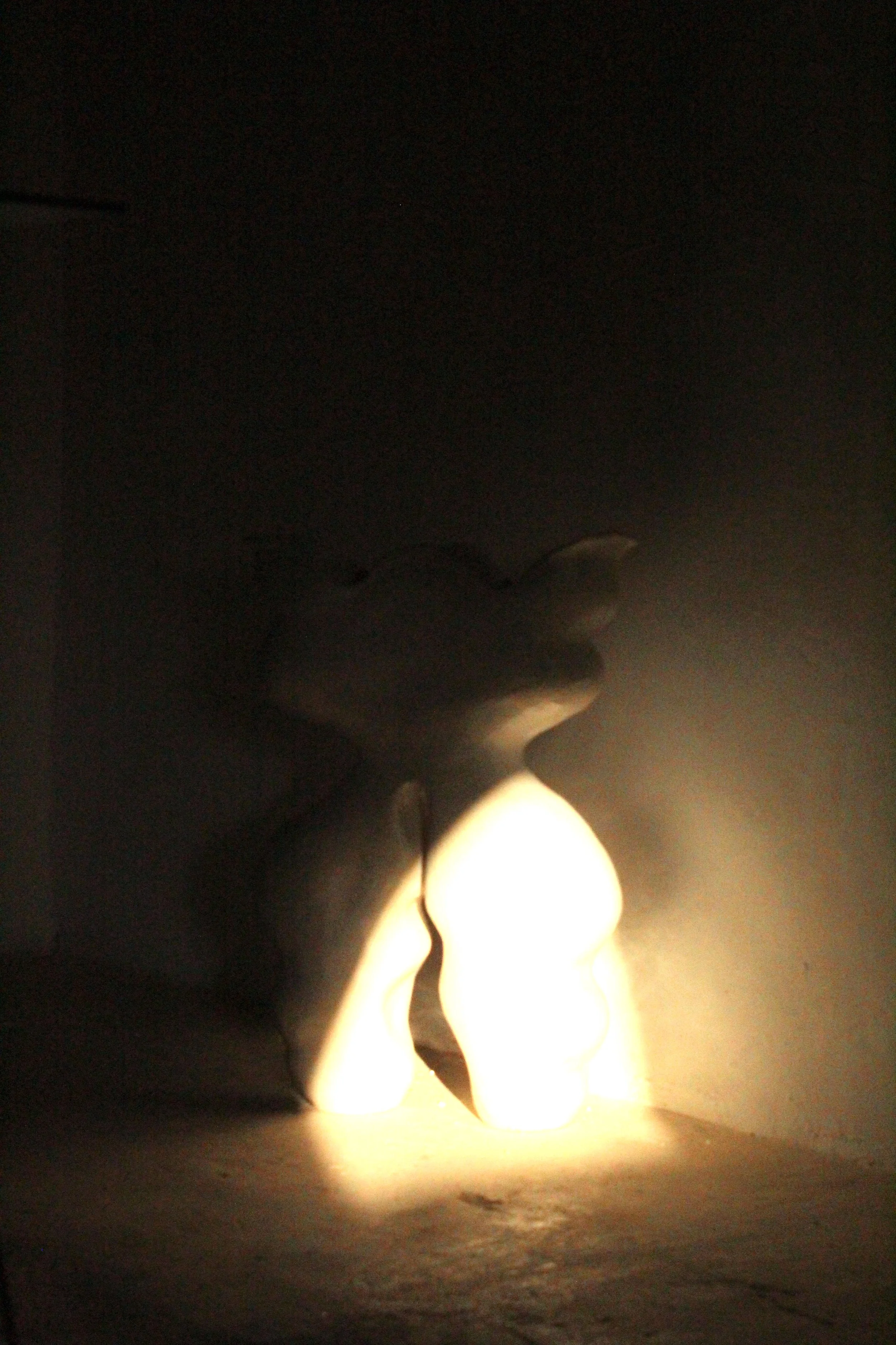 Two small candle lights illuminating a dark corner on a white surface.