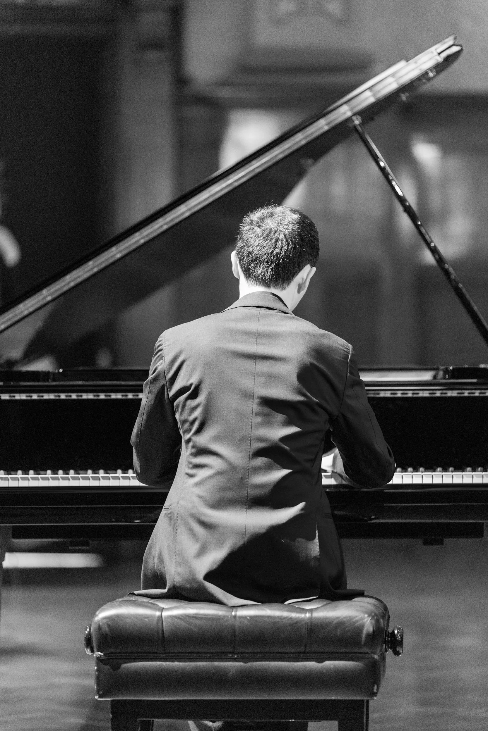 A person in formal attire playing a grand piano on stage.