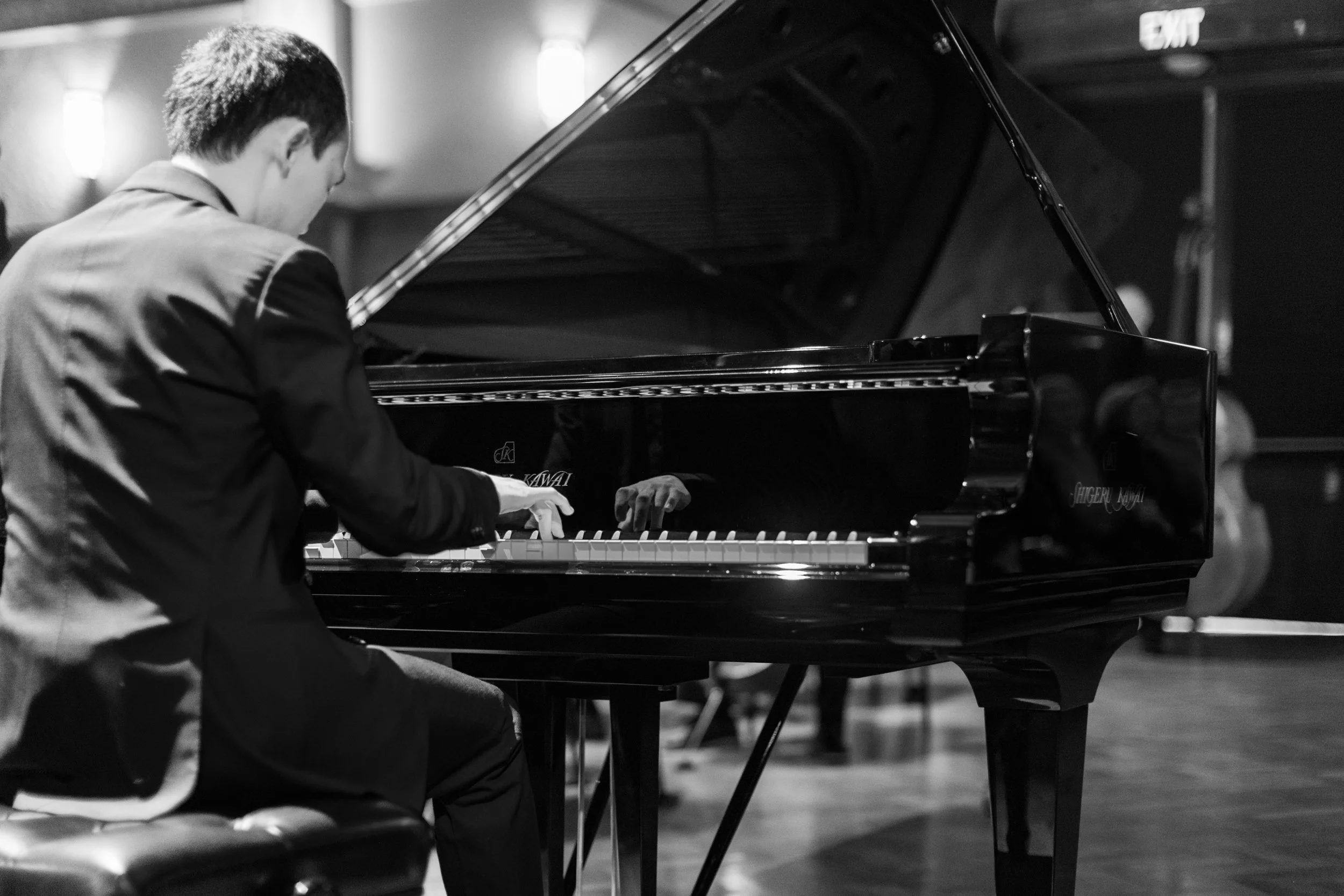 A man in a suit playing a grand piano on stage.