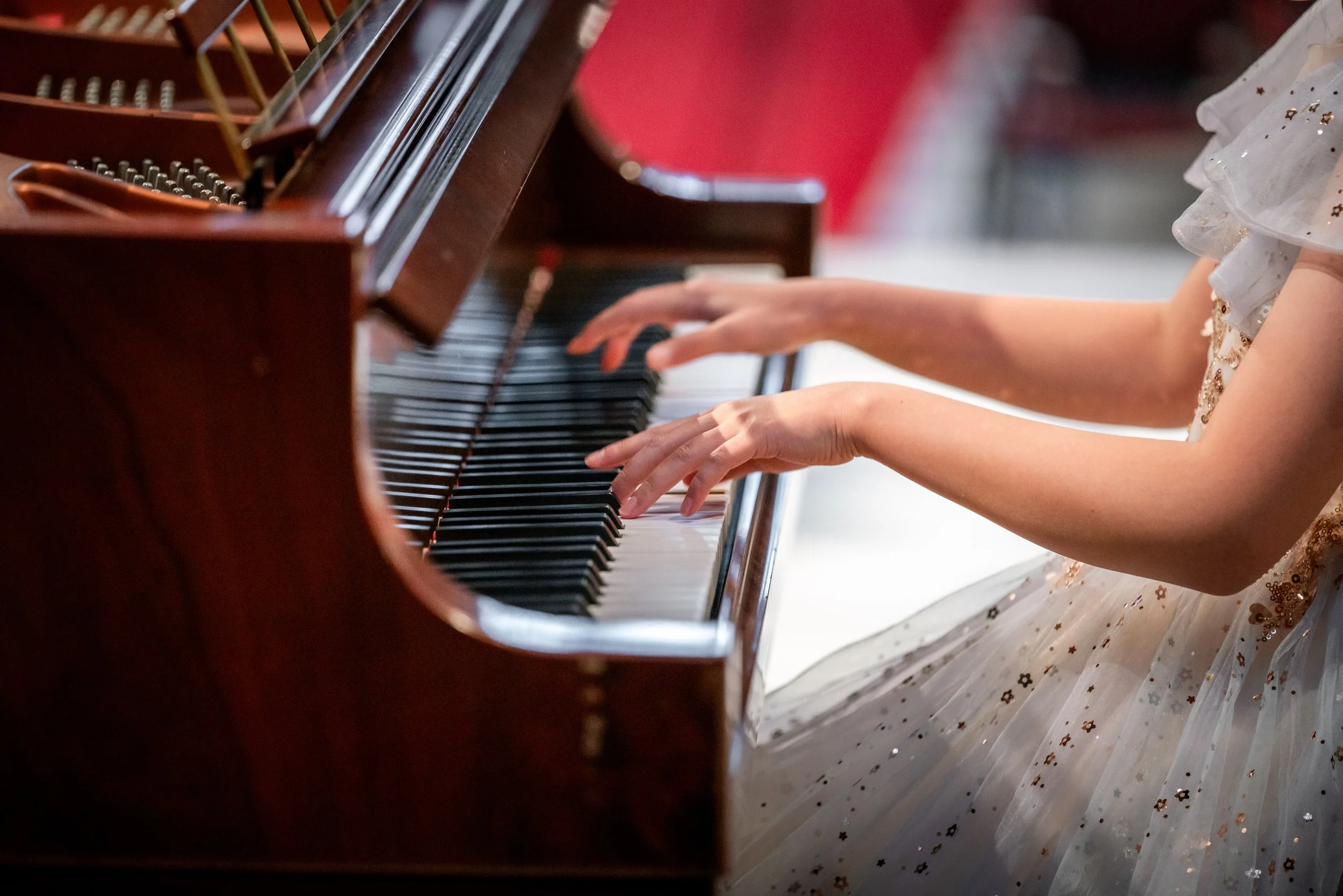 Close-up of a young girl playing the piano, wearing a white dress with gold sparkle details.