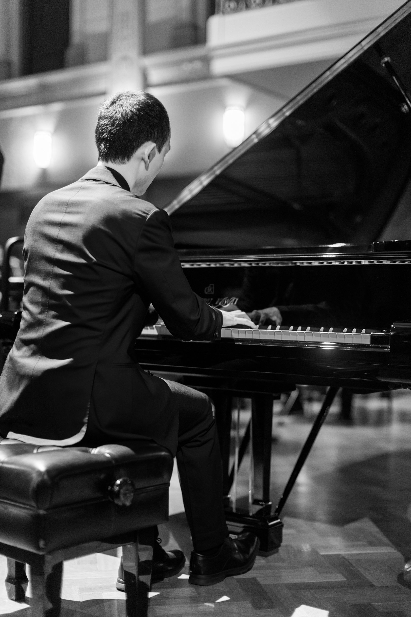 A man in a suit playing a grand piano on stage in an indoor venue.